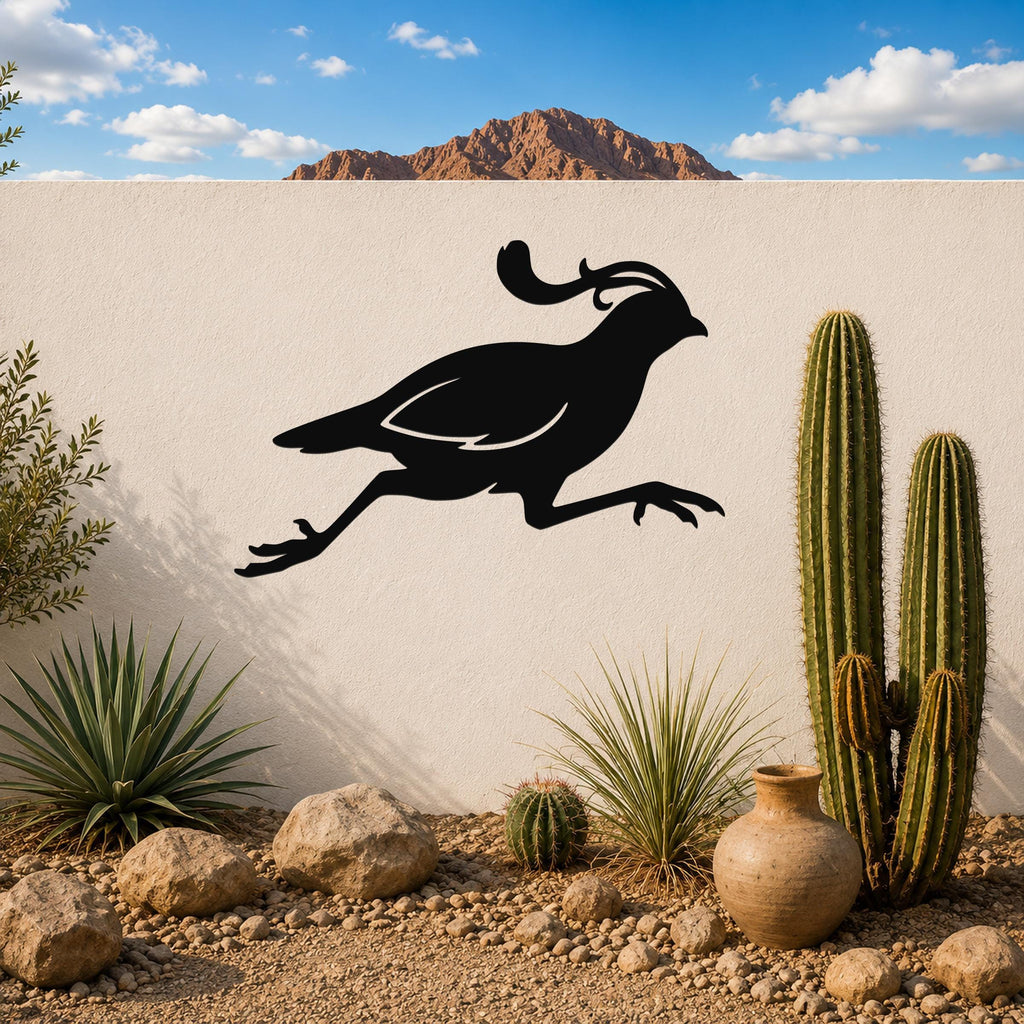 Black metal quail wall art in a running silhouette, mounted on a white outdoor wall above a desert garden with cacti and rocks.