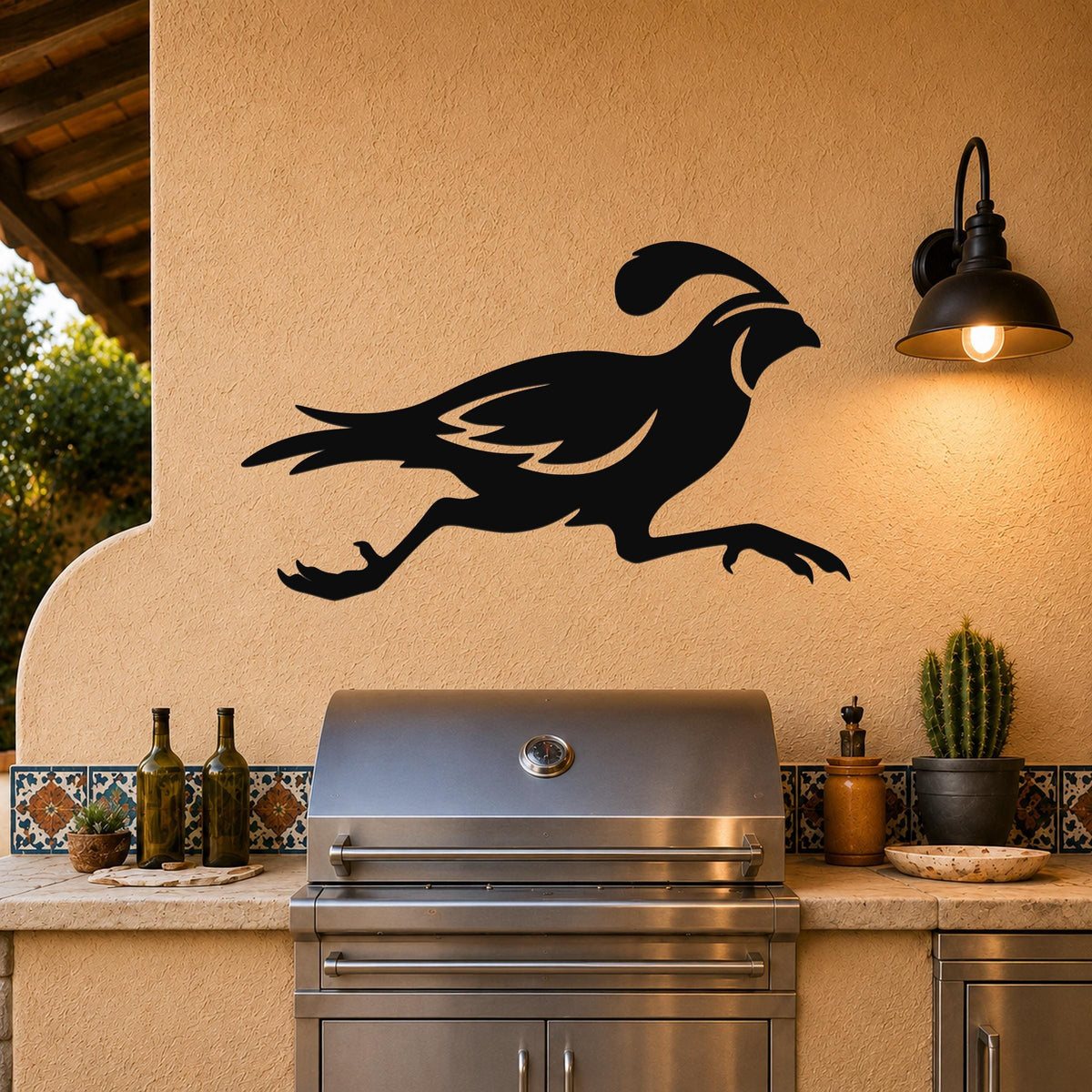Black metal quail wall art in a running silhouette, mounted on an outdoor patio wall above a stainless steel grill.