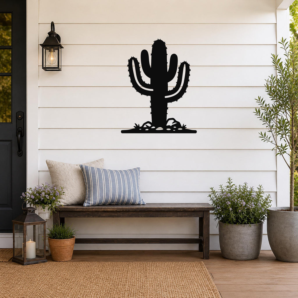 Black metal Saguaro cactus wall art with spines and base cutouts, mounted on a white shiplap wall above a wooden bench on a porch.
