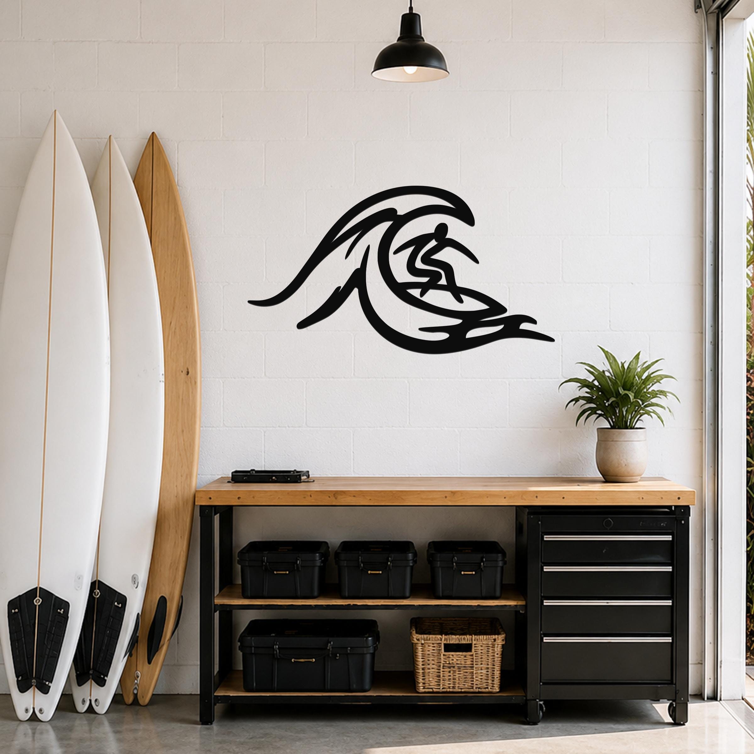 Black metal surfer wall art with wave cutout design, mounted on a white brick wall above a wooden workbench in a garage.