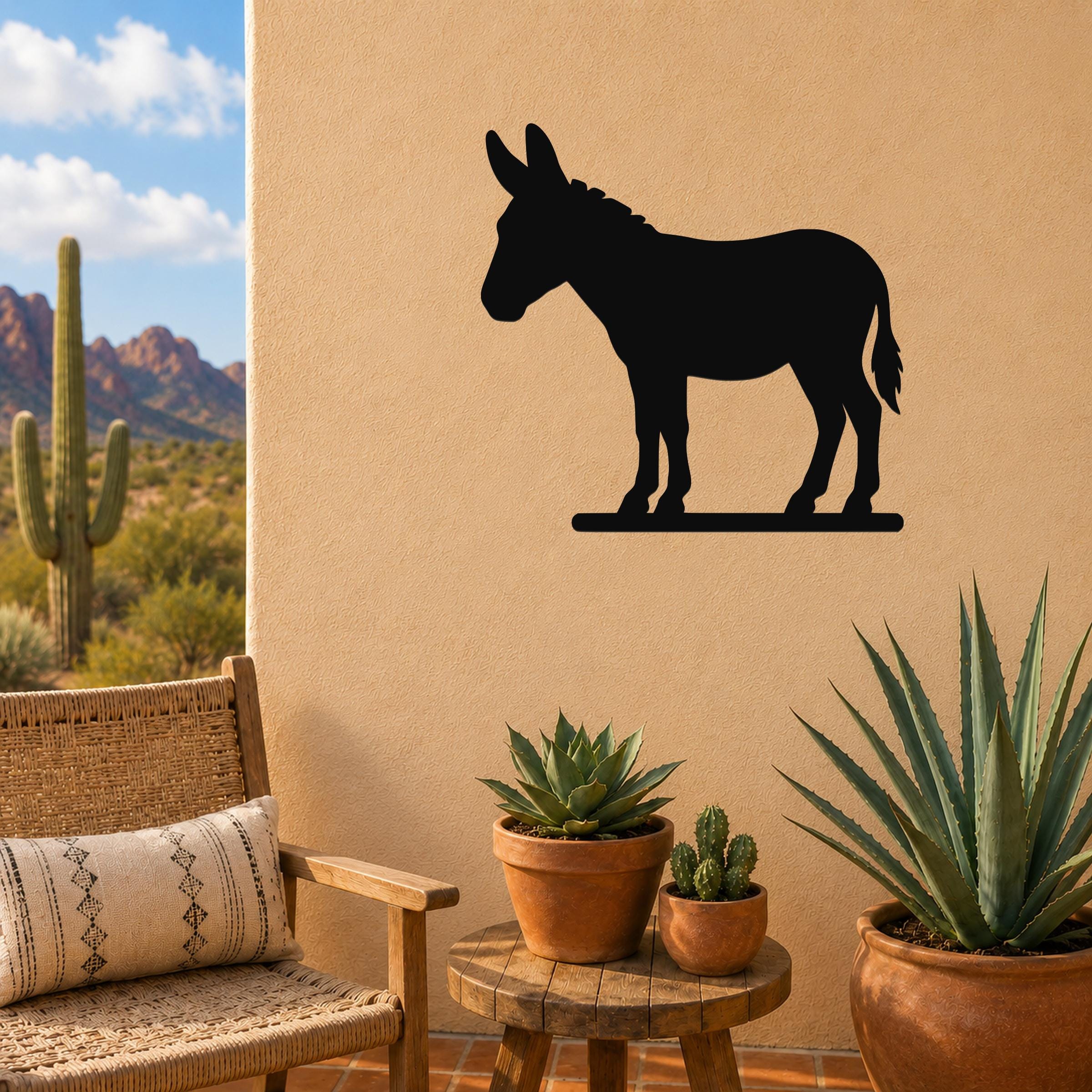 Black metal donkey silhouette wall art mounted on a beige outdoor wall above a small wooden table with potted succulents and a wicker chair.