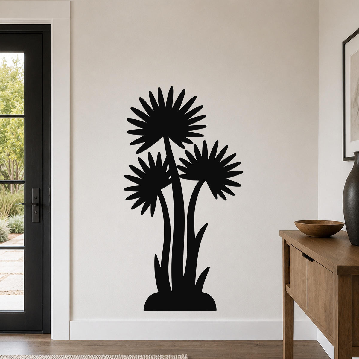 Black metal wall art featuring a silhouette of three tall wildflowers with radiating petals, mounted on a living room wall above a wooden console table.