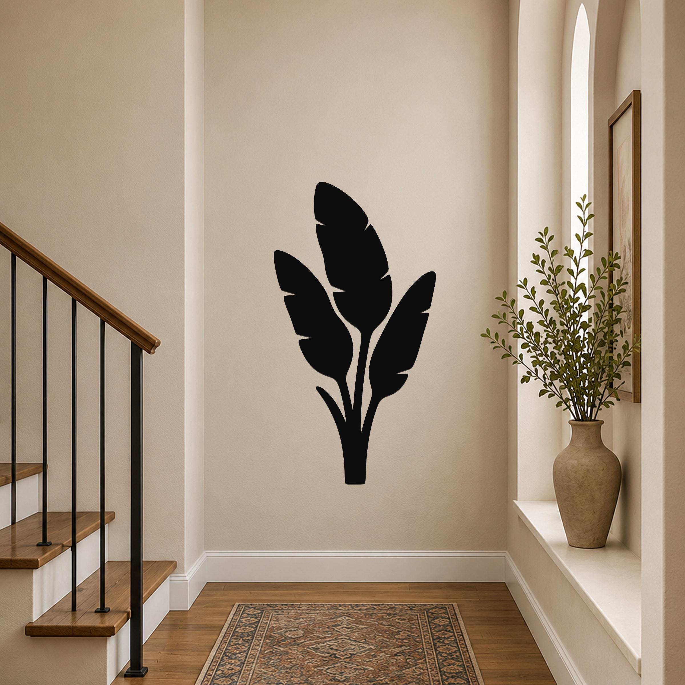 Black metal wall art with a tropical leaf silhouette, mounted on a hallway wall above a patterned rug near a staircase.