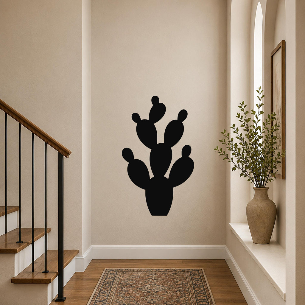 Black metal prickly pear cactus wall art with multiple pads and cutout details, mounted on a hallway wall above a patterned rug near a staircase.