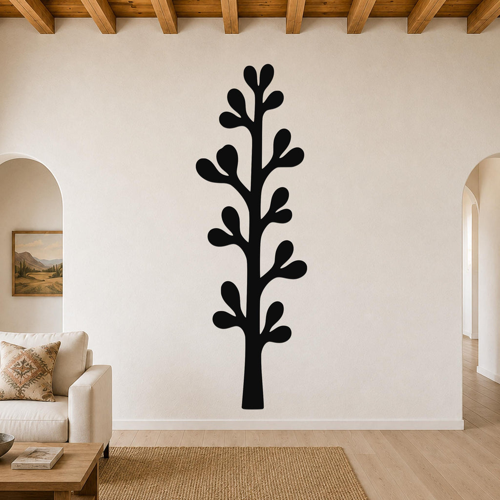 Black metal wall art in a tall, slender tree silhouette with leaf-shaped cutouts, mounted on a living room wall above a beige sofa.