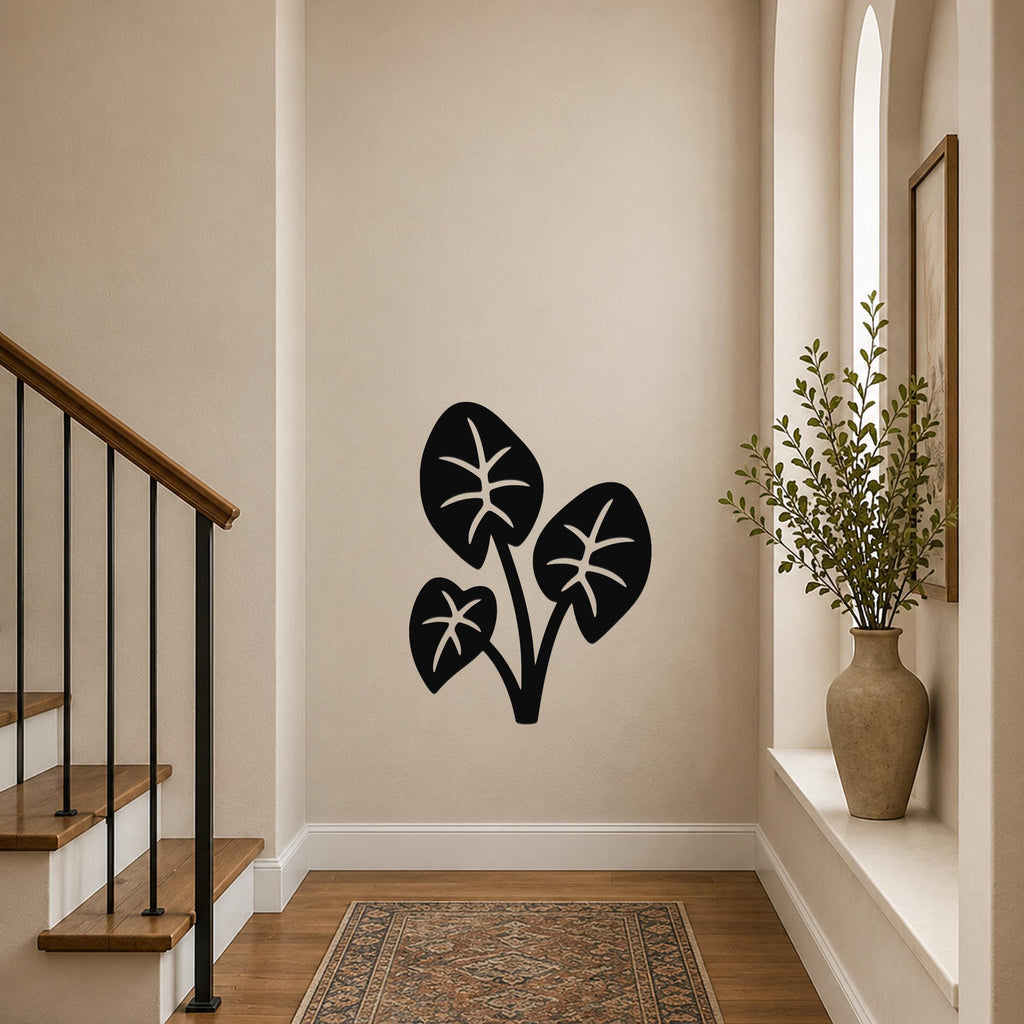 Black metal wall art in a silhouette of three elephant ear leaves with internal vein cutouts, mounted on a hallway wall near a staircase and a vase with greenery.