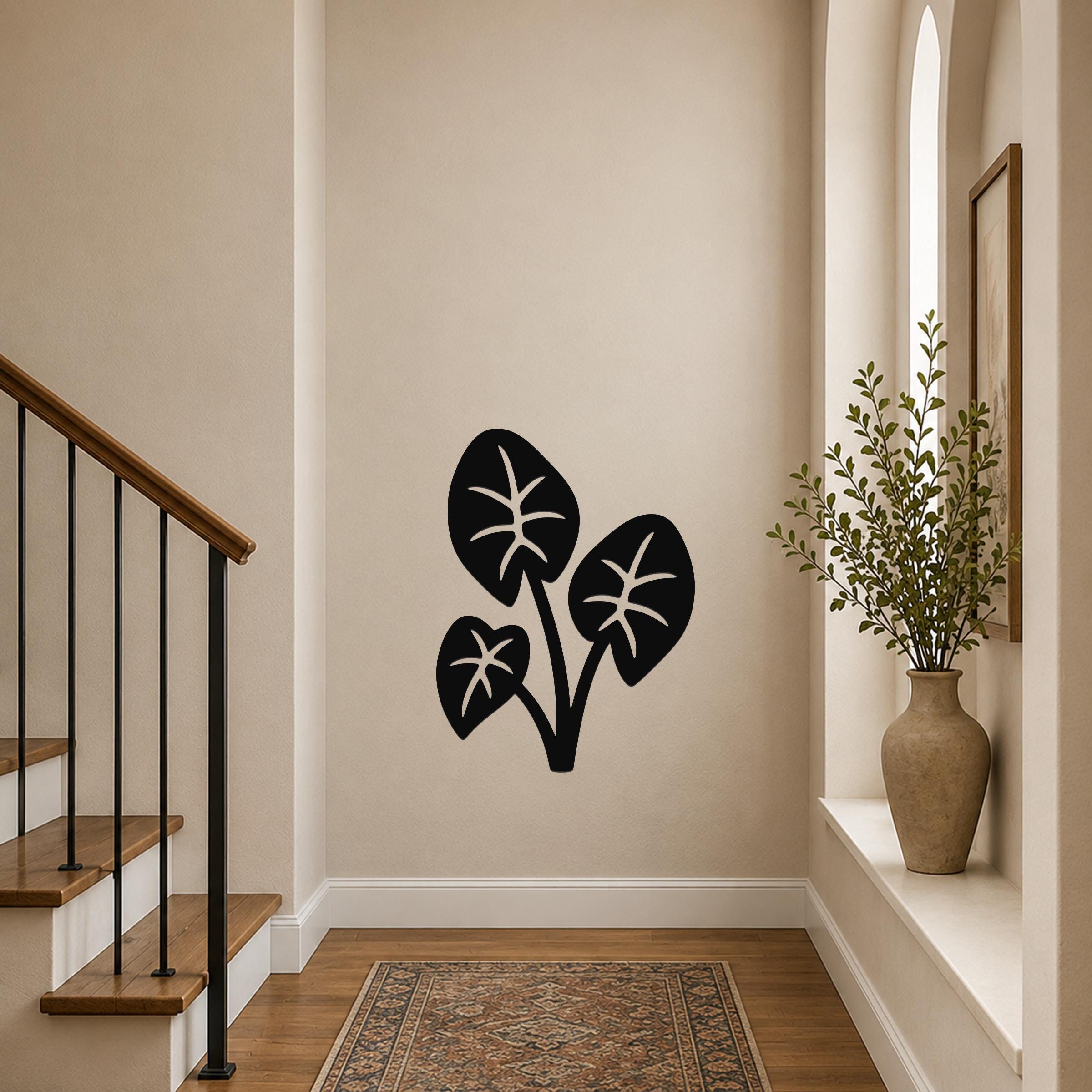 Black metal wall art in a silhouette of three elephant ear leaves with internal vein cutouts, mounted on a hallway wall near a staircase and a vase with greenery.