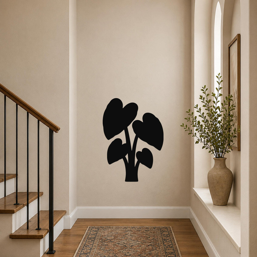 Black metal wall art silhouette of an elephant ear plant with large heart-shaped leaves, mounted on a beige hallway wall near a staircase and window.