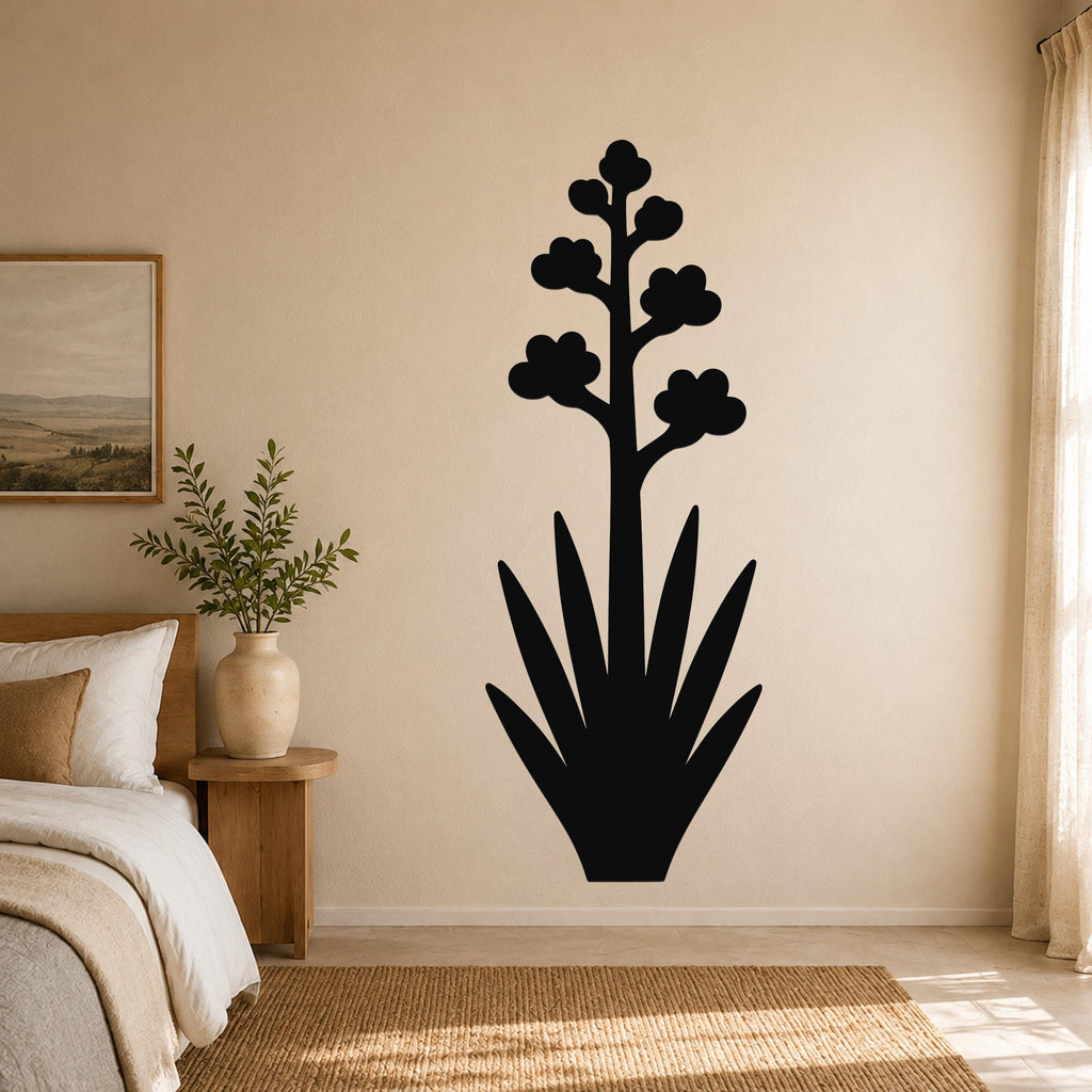Black metal agave wall art with blooming flower silhouette, mounted on a beige bedroom wall above a woven rug.