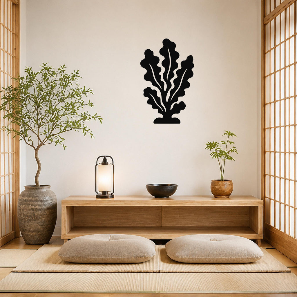 Black metal kelp wall art with leafy cutouts, mounted on a beige wall above a wooden console in a minimalist room.