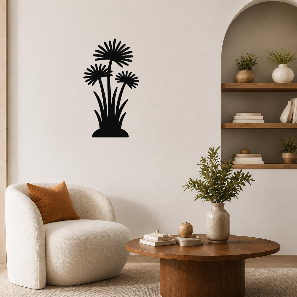 Black metal wall art featuring a silhouette of three daisy-like flowers with long stems and leaves, mounted on a living room wall above a round wooden coffee table.