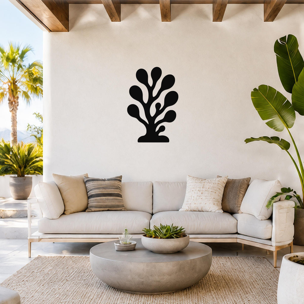Black metal wall art in a coral or seaweed silhouette with multiple rounded lobes, mounted on a white wall above a light-colored sofa in a bright living room.
