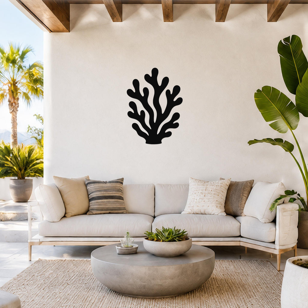 Black metal coral wall art with branching cutouts, mounted on a white wall above a light-colored sofa in a bright outdoor living space.