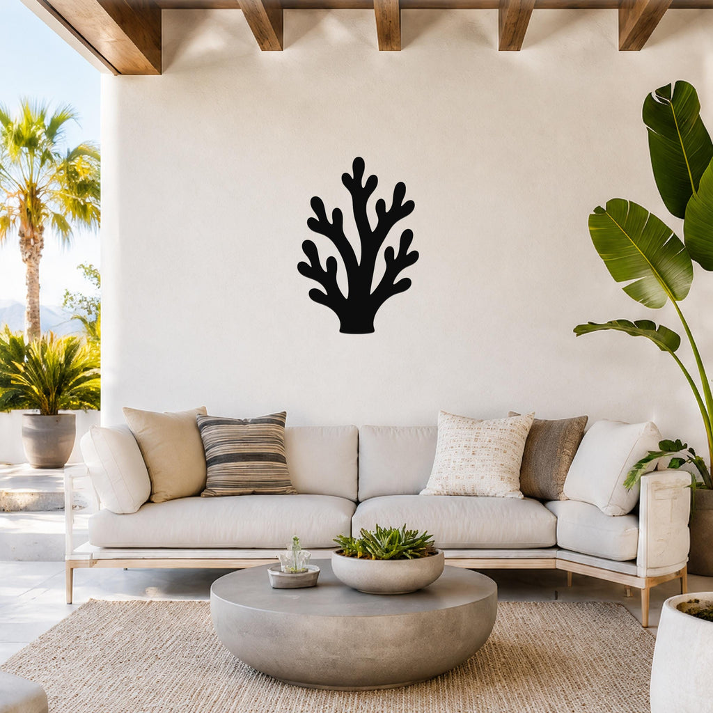 Black metal branching coral wall art with intricate cutout details, mounted on a white wall above a light-colored sofa in a bright living room.