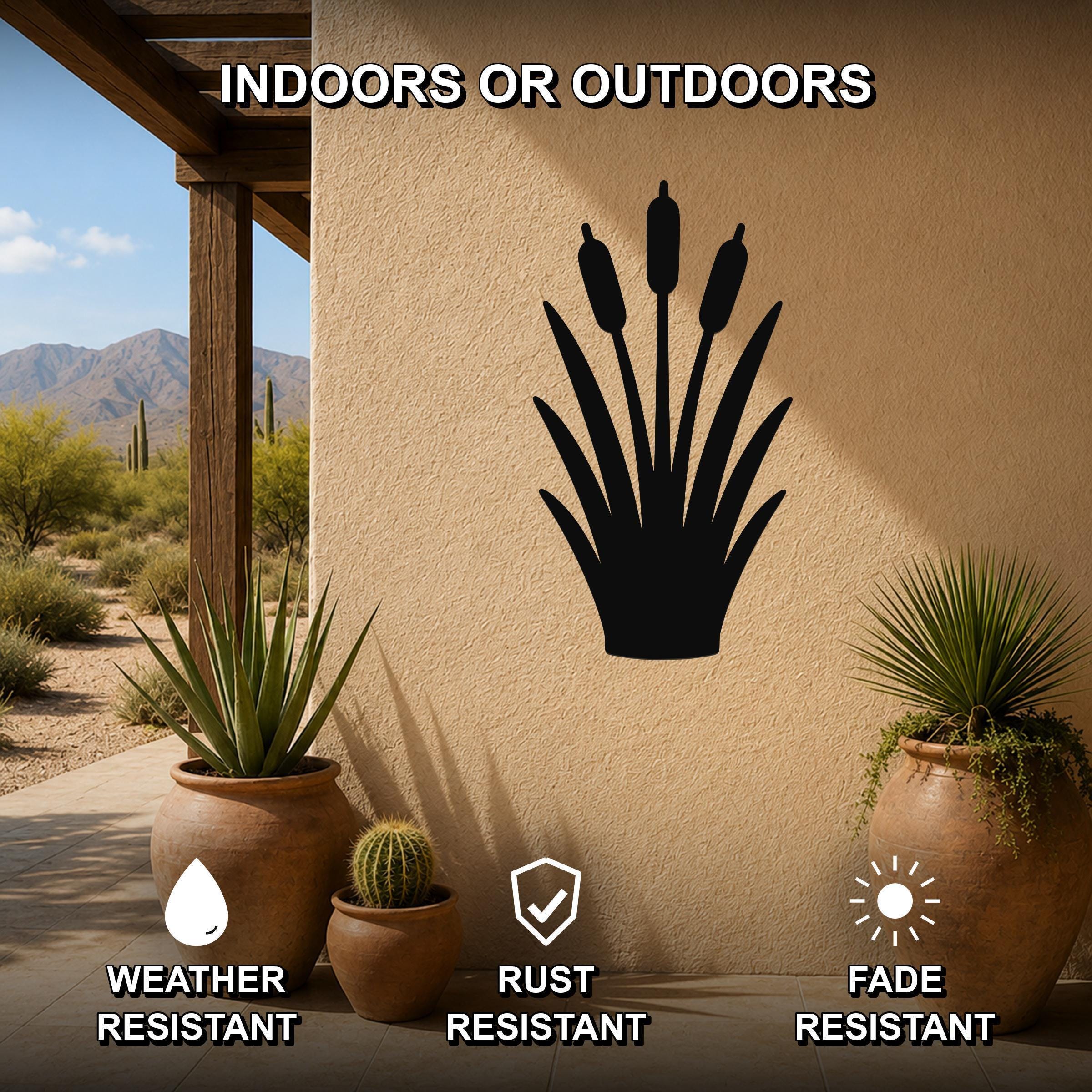 Black metal cattail wall art silhouette mounted on a beige outdoor wall, displayed on a patio with potted plants and desert scenery in the background.