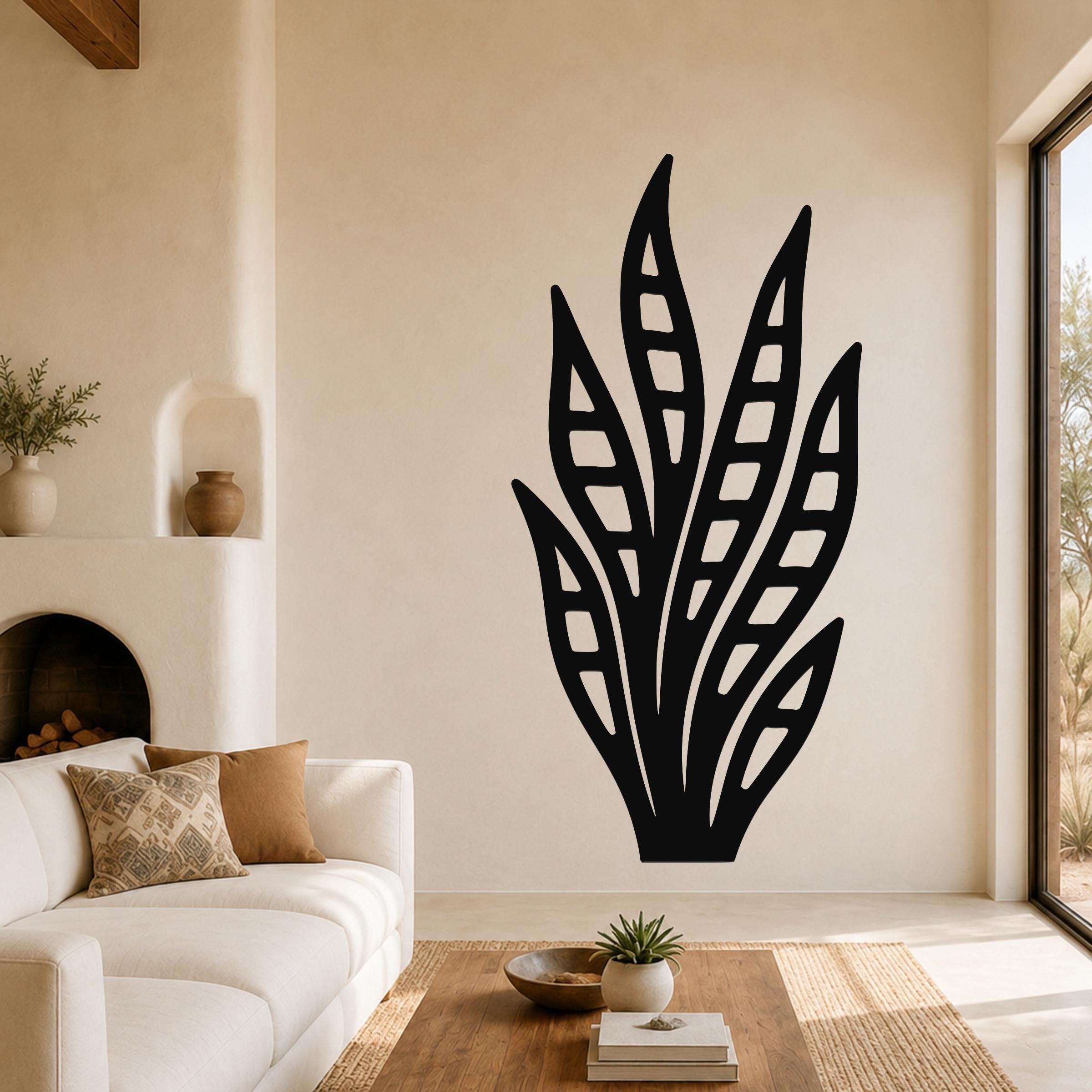 Black metal wall art in a snake plant silhouette with internal leaf cutouts, mounted on a living room wall above a white sofa.