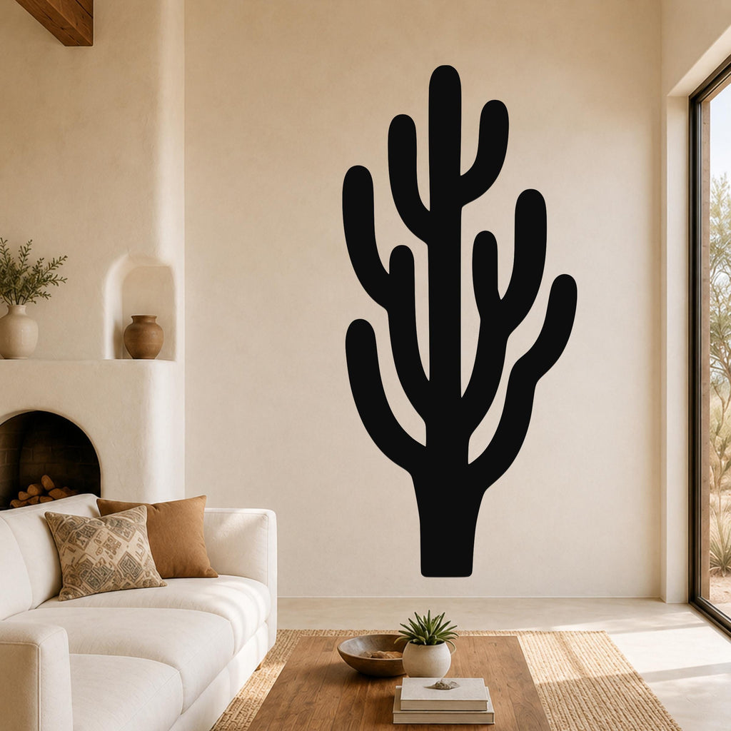 Black metal saguaro cactus wall art with branching cutouts, mounted on a living room wall above a white sofa.