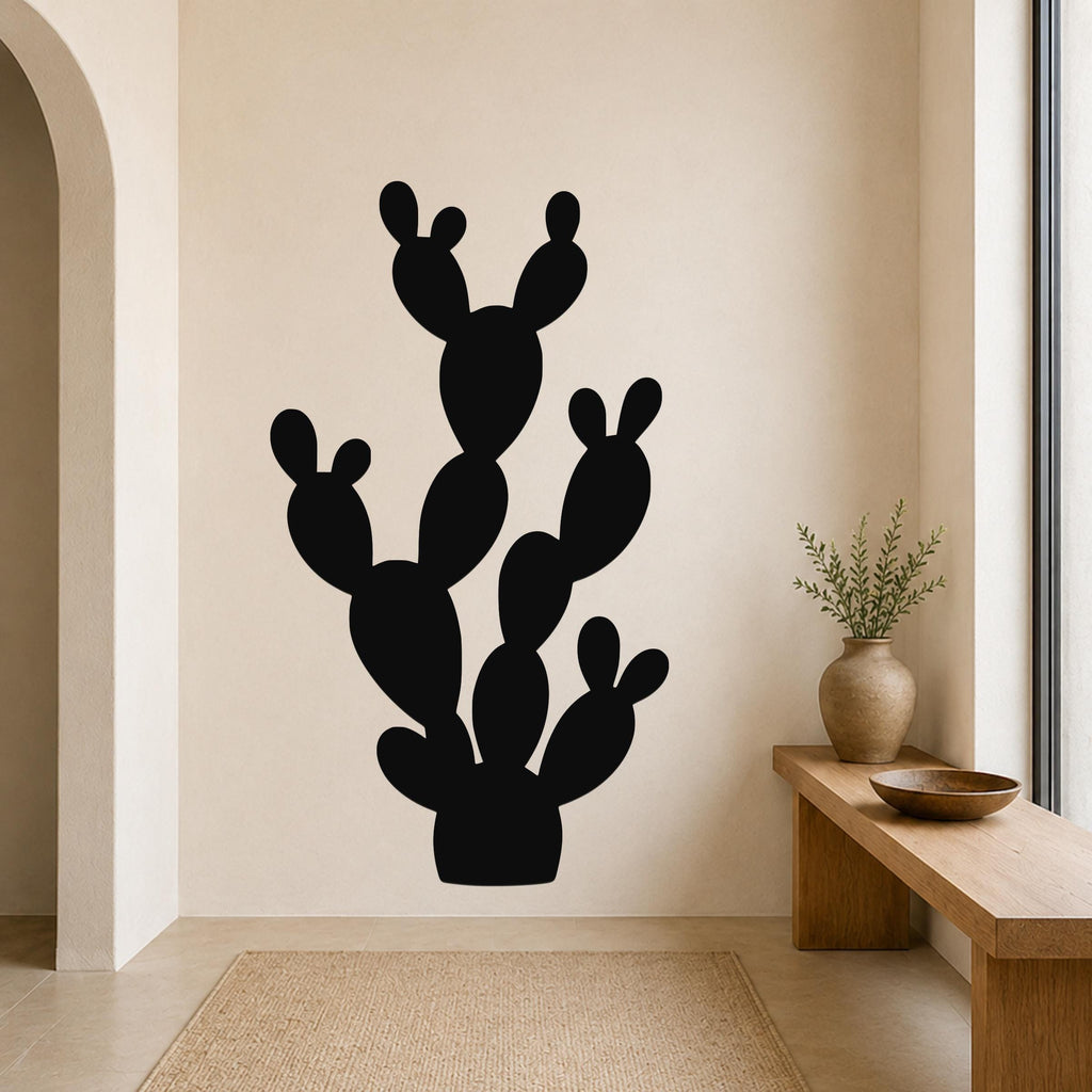 Black metal wall art in the silhouette of a prickly pear cactus with multiple pads and arms, mounted on a beige wall above a wooden bench in a minimalist entryway.