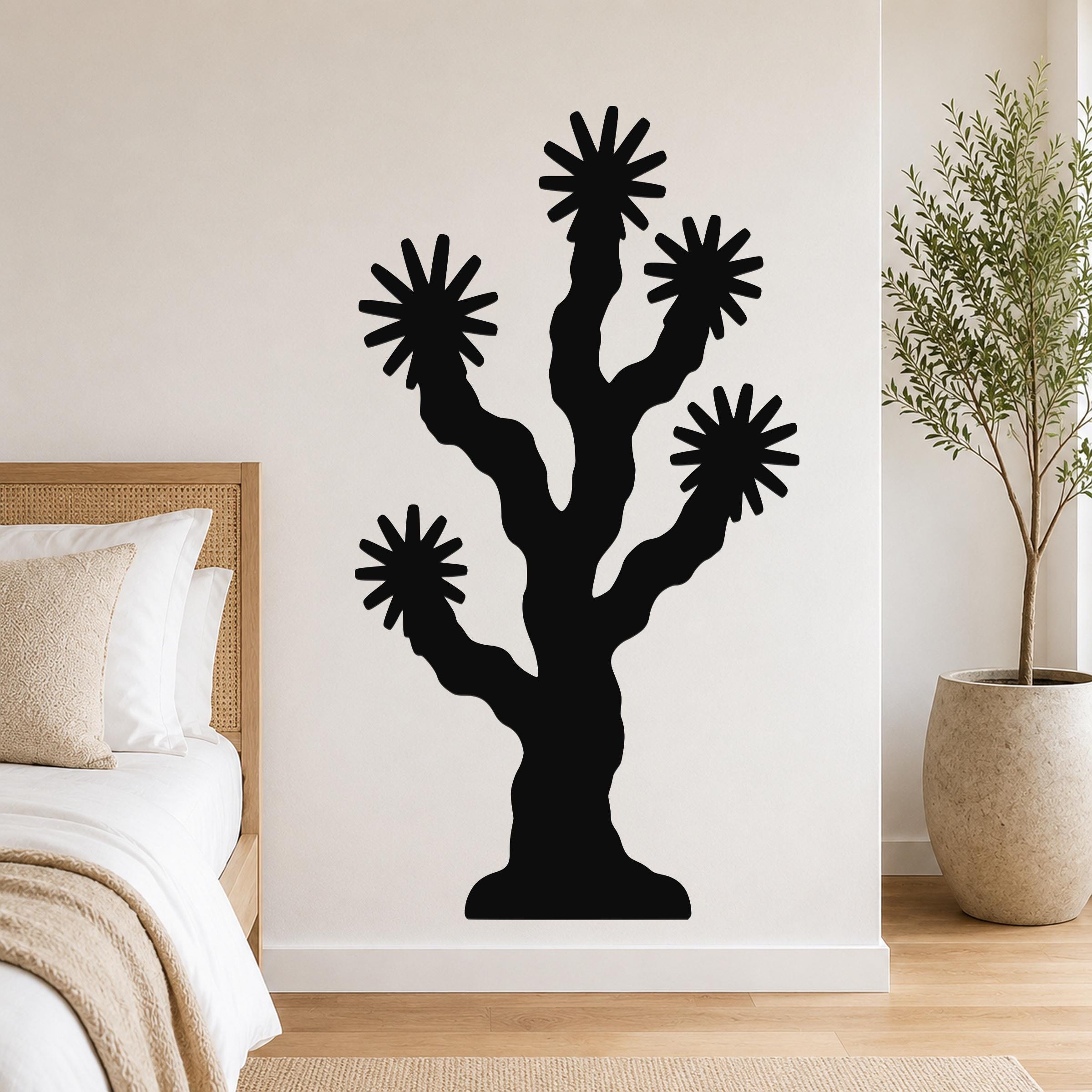 Black metal Joshua tree wall art with starburst cutouts, mounted on a bedroom wall above a bed.