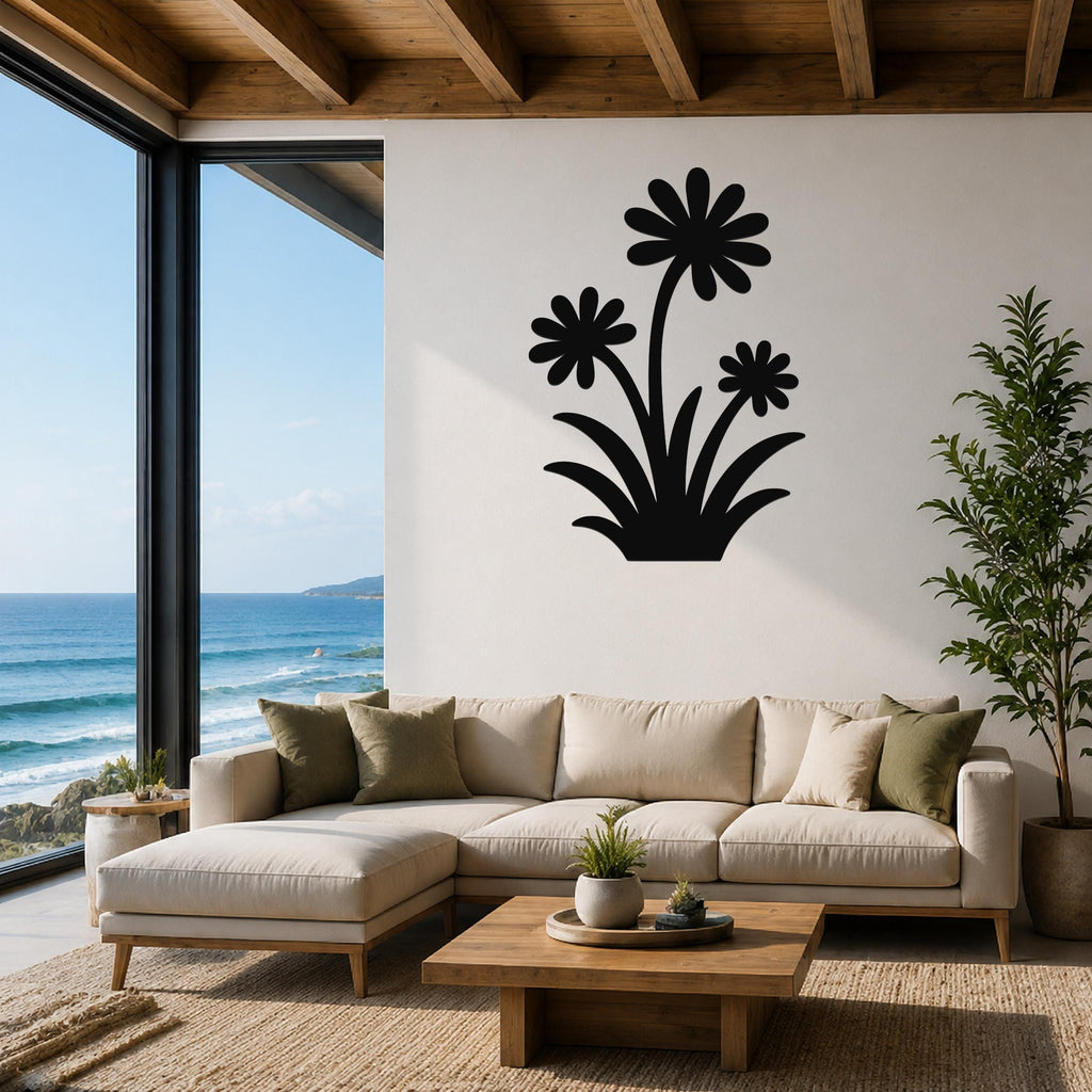 Black metal wall art with a wildflower silhouette of three daisies and leaves, mounted on a white wall above a beige sofa in a living room with ocean views.