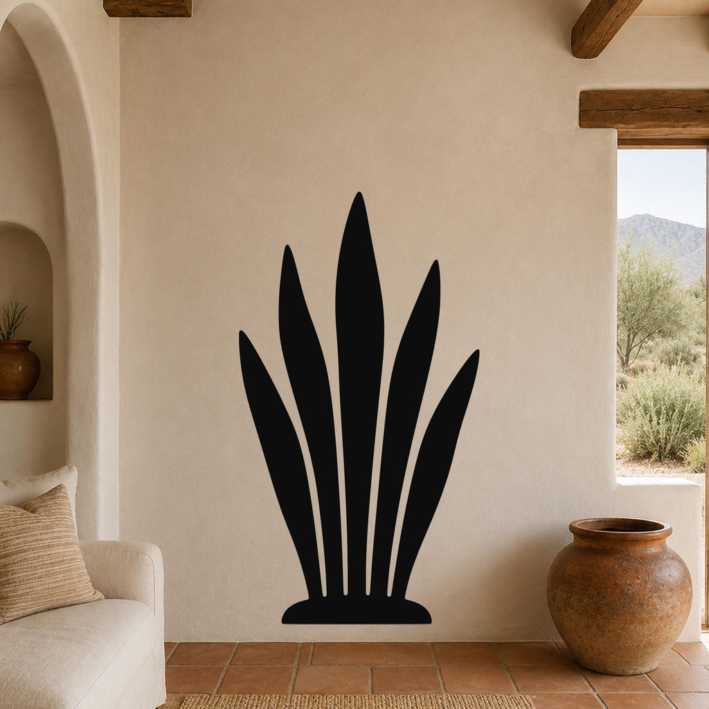 Black metal agave plant wall art with leaf cutouts, mounted on a beige living room wall above a terracotta-tiled floor.