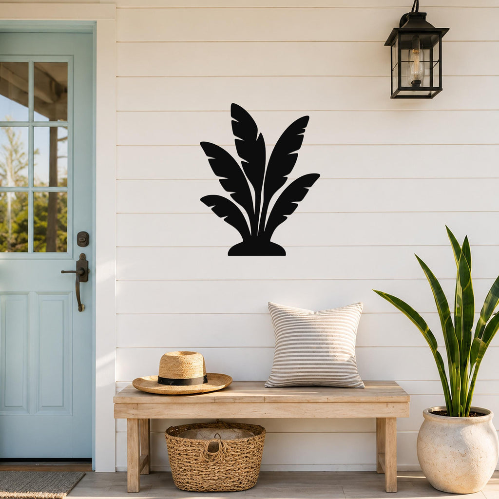 Black metal tropical leaves wall art silhouette mounted on a white shiplap wall above a wooden bench in a porch entryway.