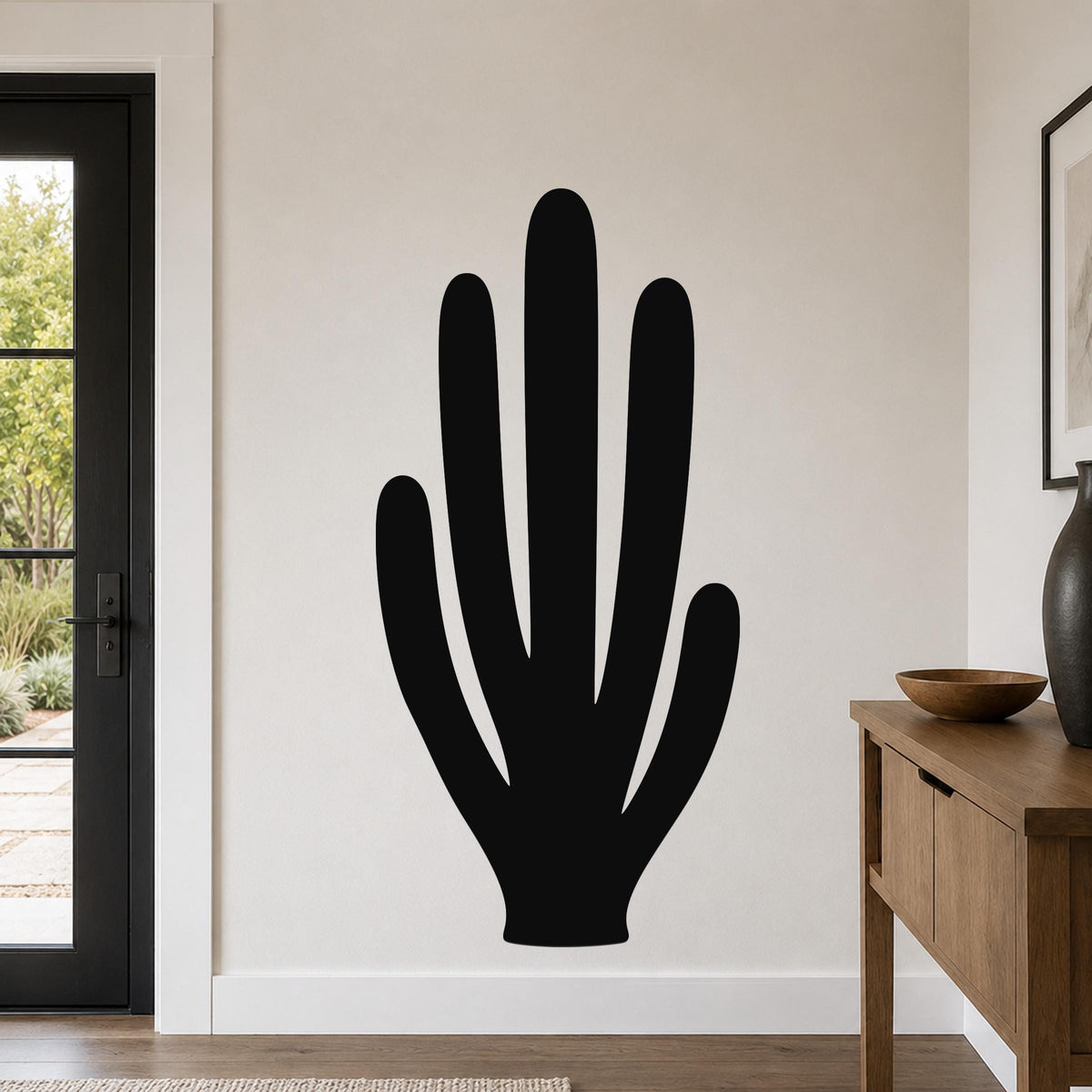 Black metal wall art in the silhouette of an organ pipe cactus, mounted on a light-colored wall in a modern living room.