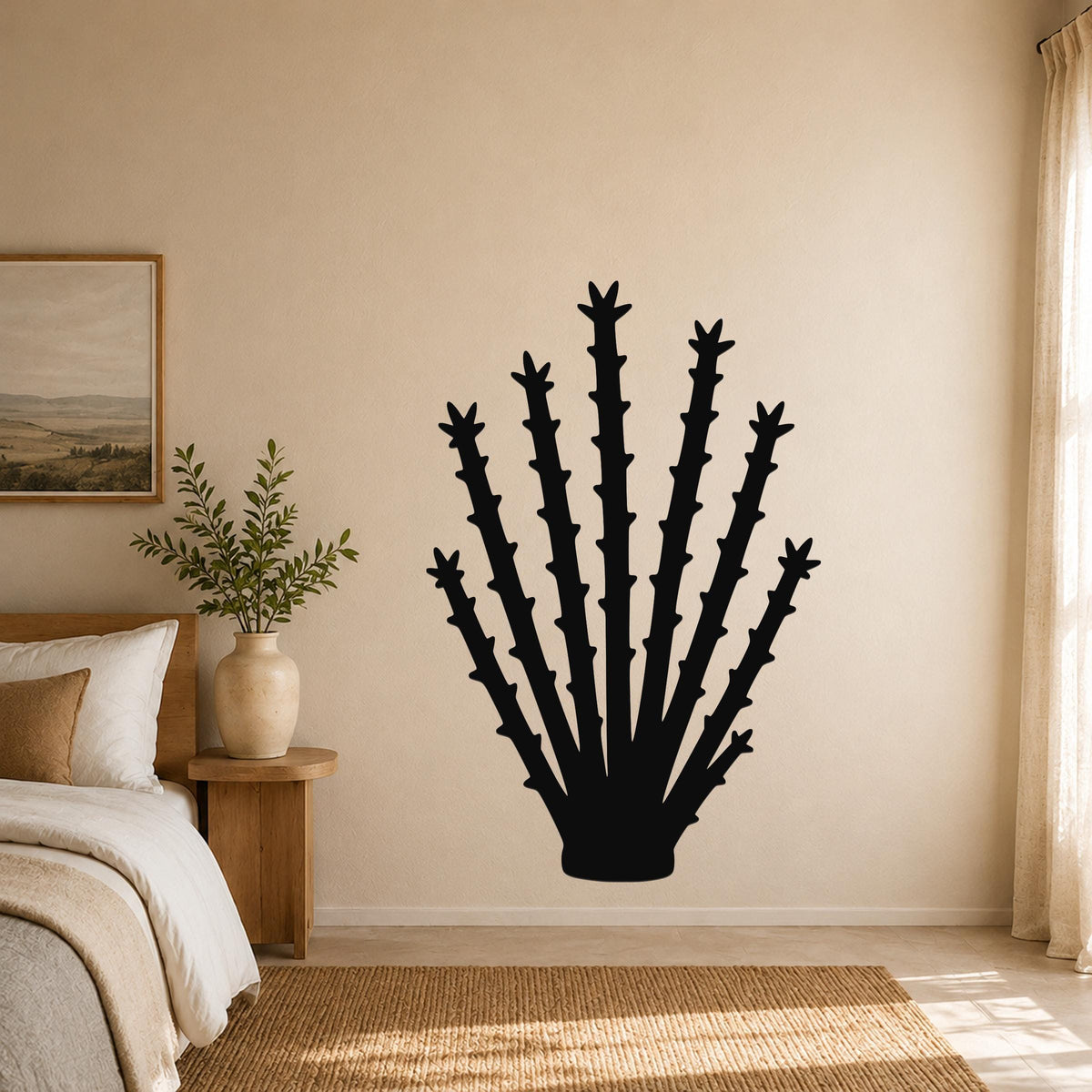 Black metal ocotillo wall art silhouette with spiky branches, mounted on a beige bedroom wall above a woven rug.