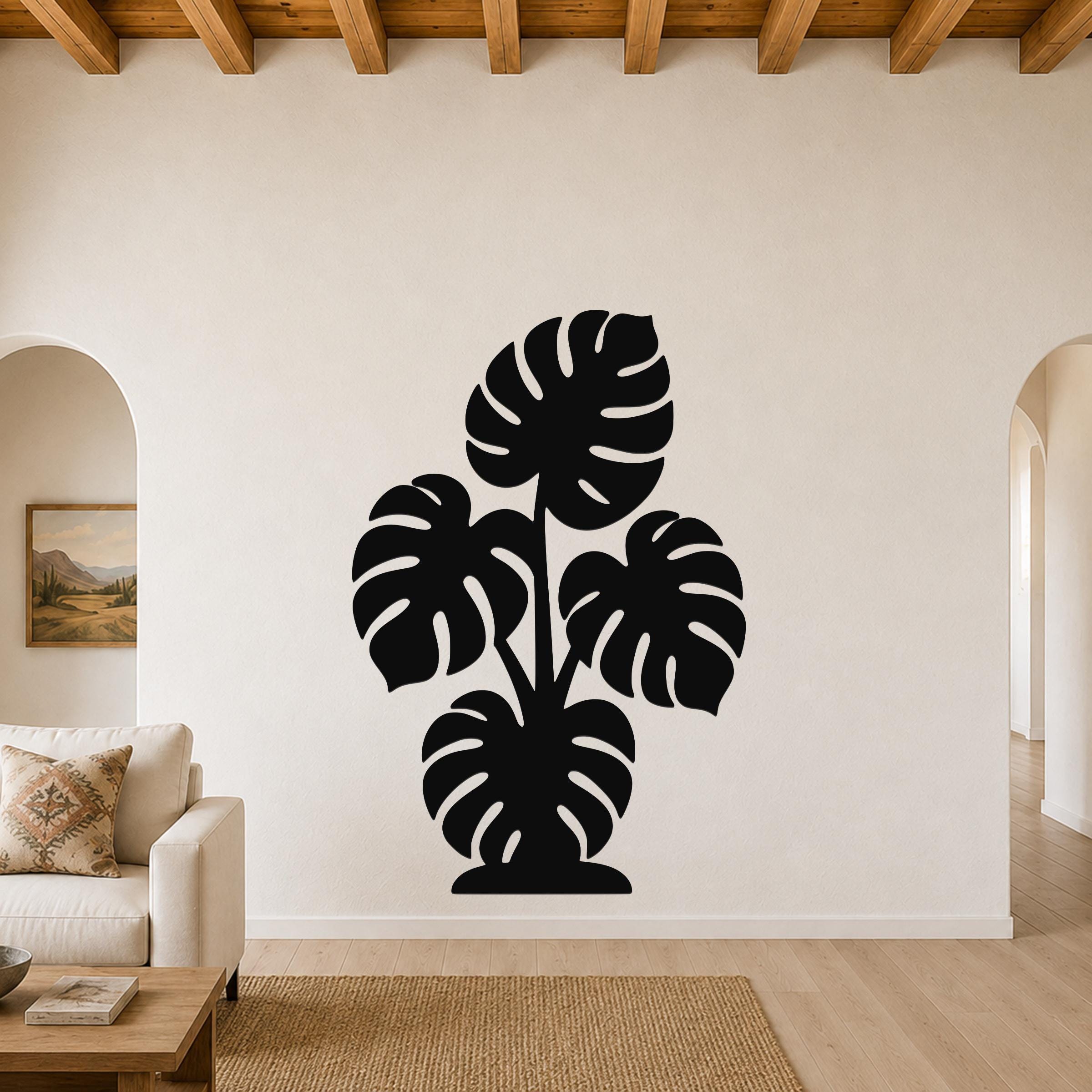 Black metal wall art cutout of a monstera plant with large leaf openings, mounted on a living room wall above a sofa.