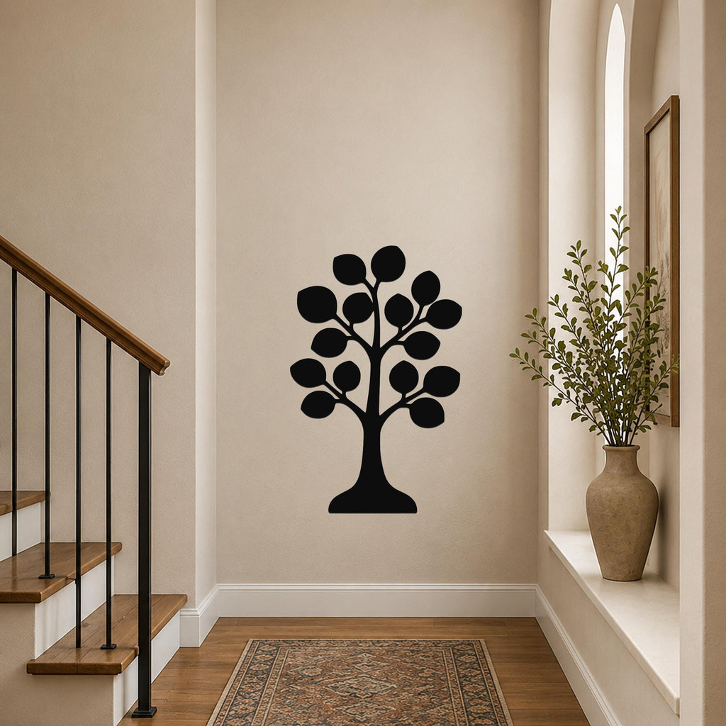 Black metal tree wall art with leaf cutouts, mounted on a hallway wall near a staircase and a vase with greenery.