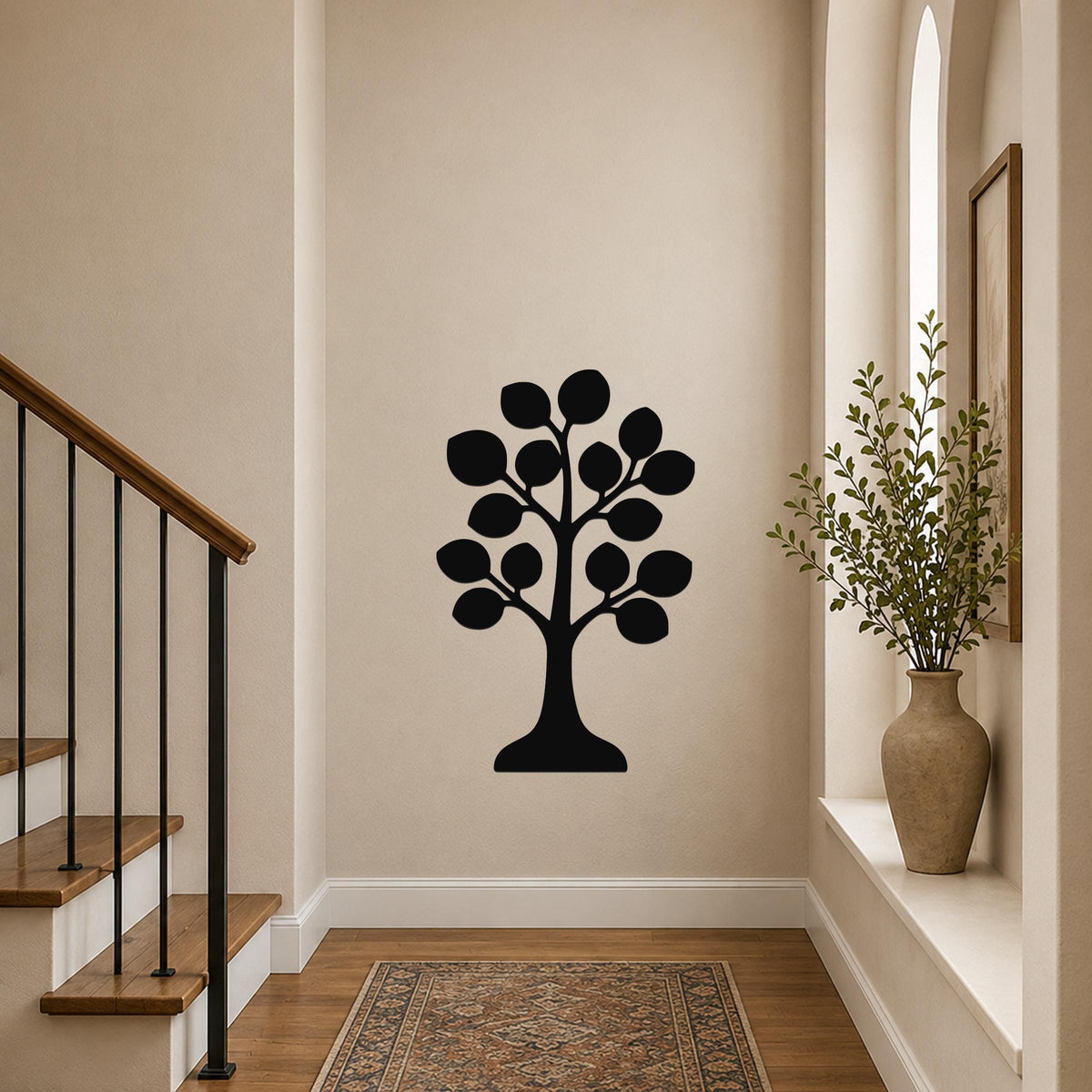 Black metal tree wall art with leaf cutouts, mounted on a hallway wall near a staircase and a vase with greenery.