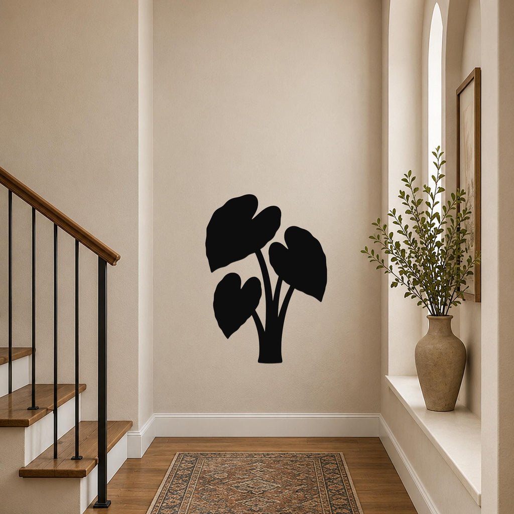 Black metal wall art in the silhouette of an elephant ear plant, mounted on a beige hallway wall above a patterned rug near a staircase.