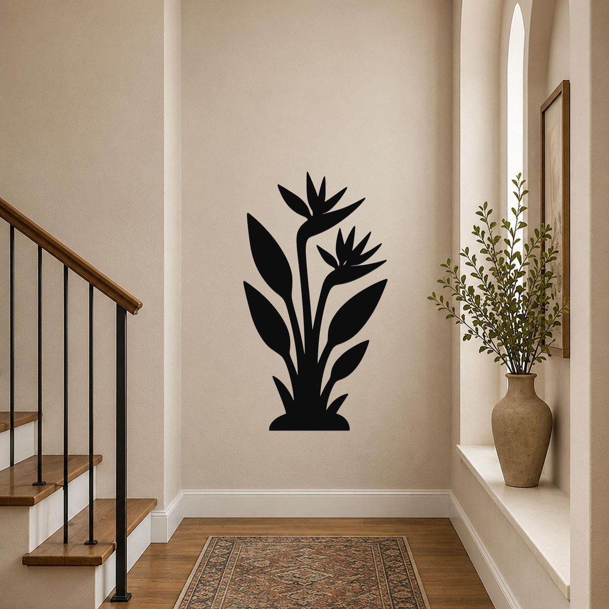 Black metal wall art silhouette of a bird of paradise plant with layered leaves and flowers, mounted on a hallway wall above a patterned rug.