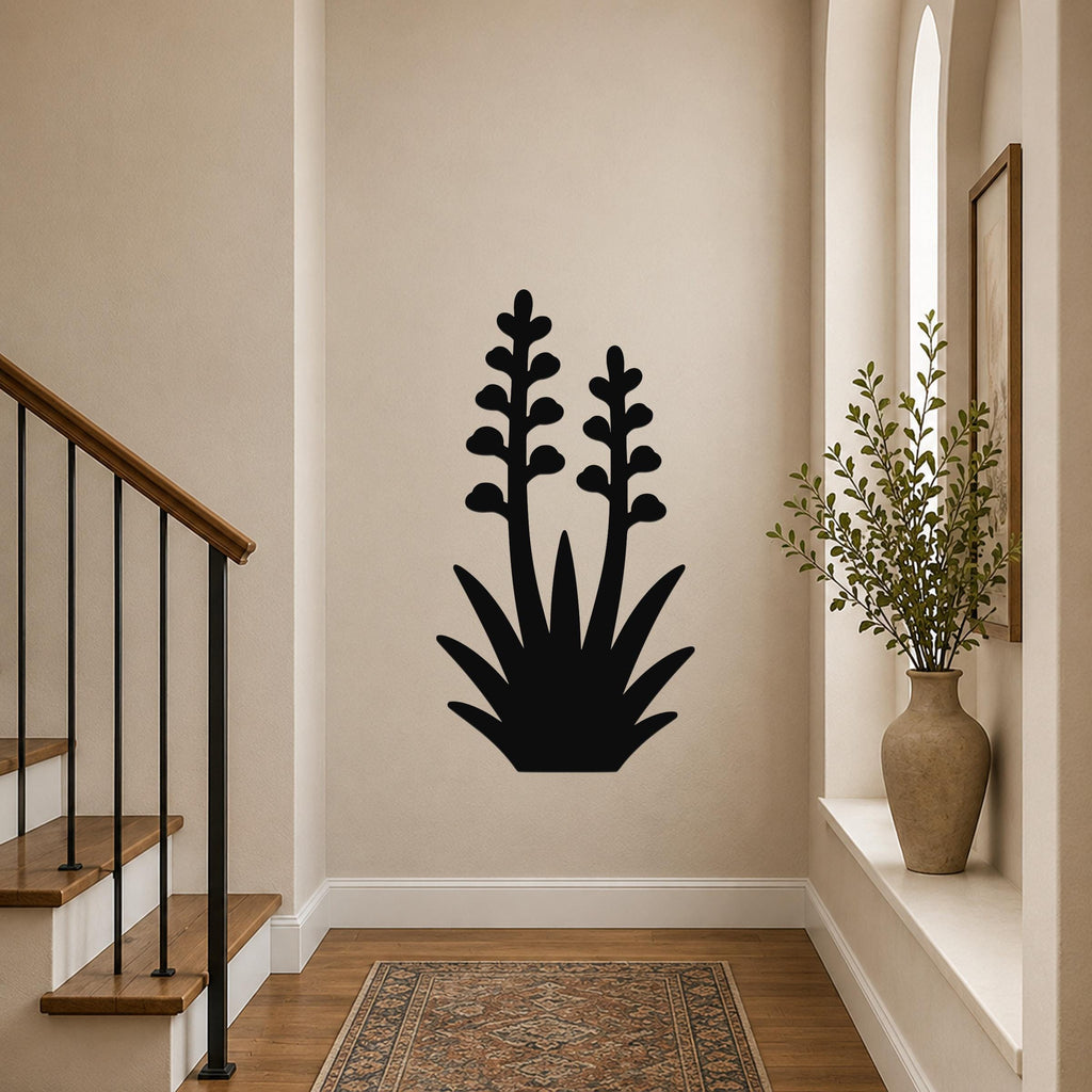 Black metal wall art in the silhouette of a blooming agave plant with two tall flower stalks, mounted on a hallway wall above a patterned rug.