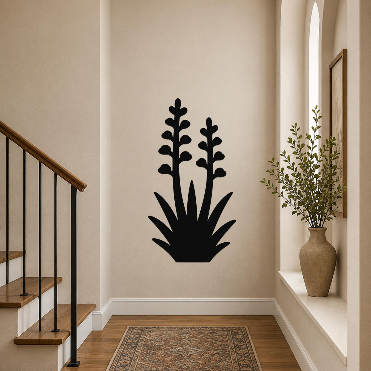 Black metal wall art in the silhouette of a blooming agave plant with two tall flower stalks, mounted on a hallway wall above a patterned rug.