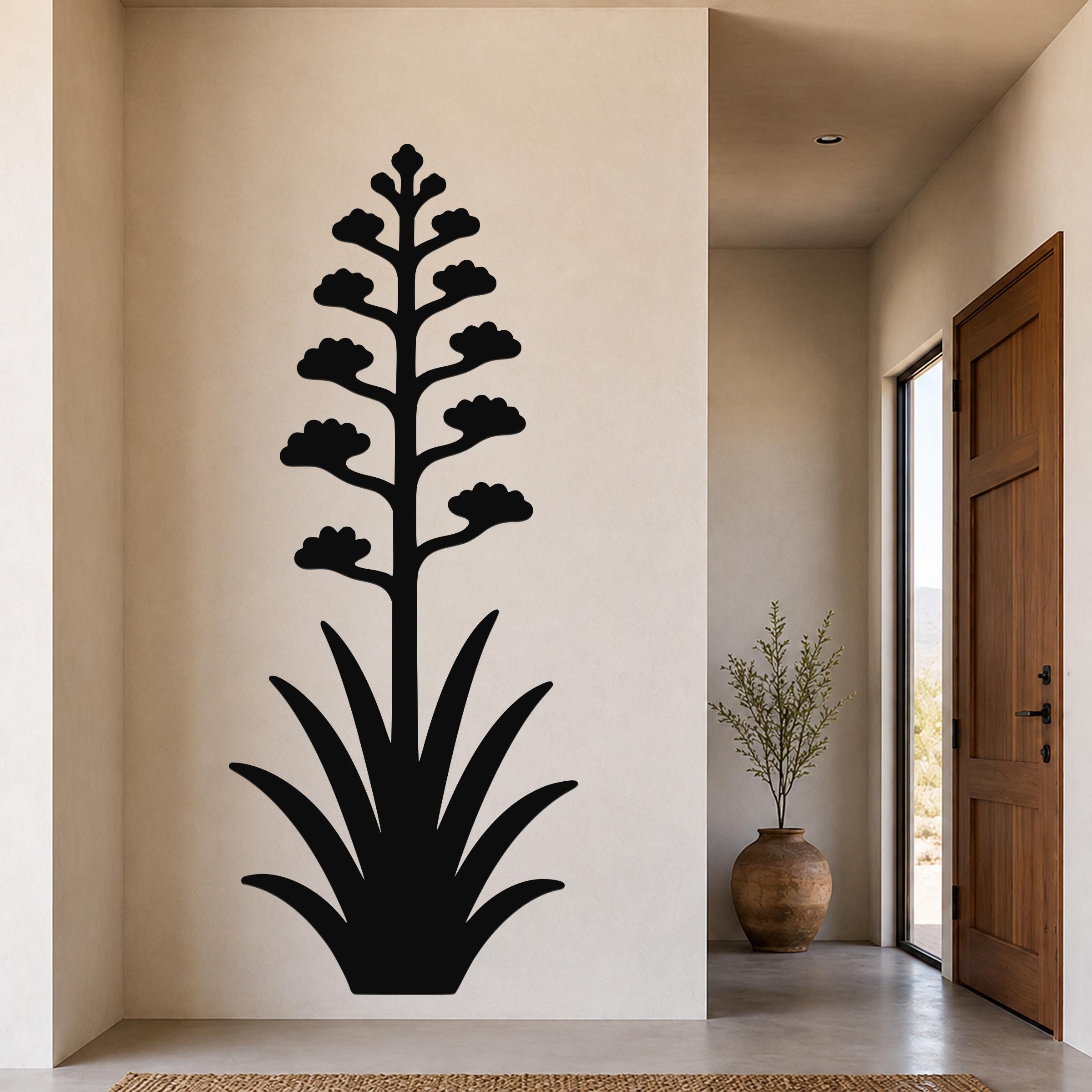 Black metal wall art in the silhouette of a blooming agave plant, mounted on a beige wall in a hallway near a wooden door and a potted plant.