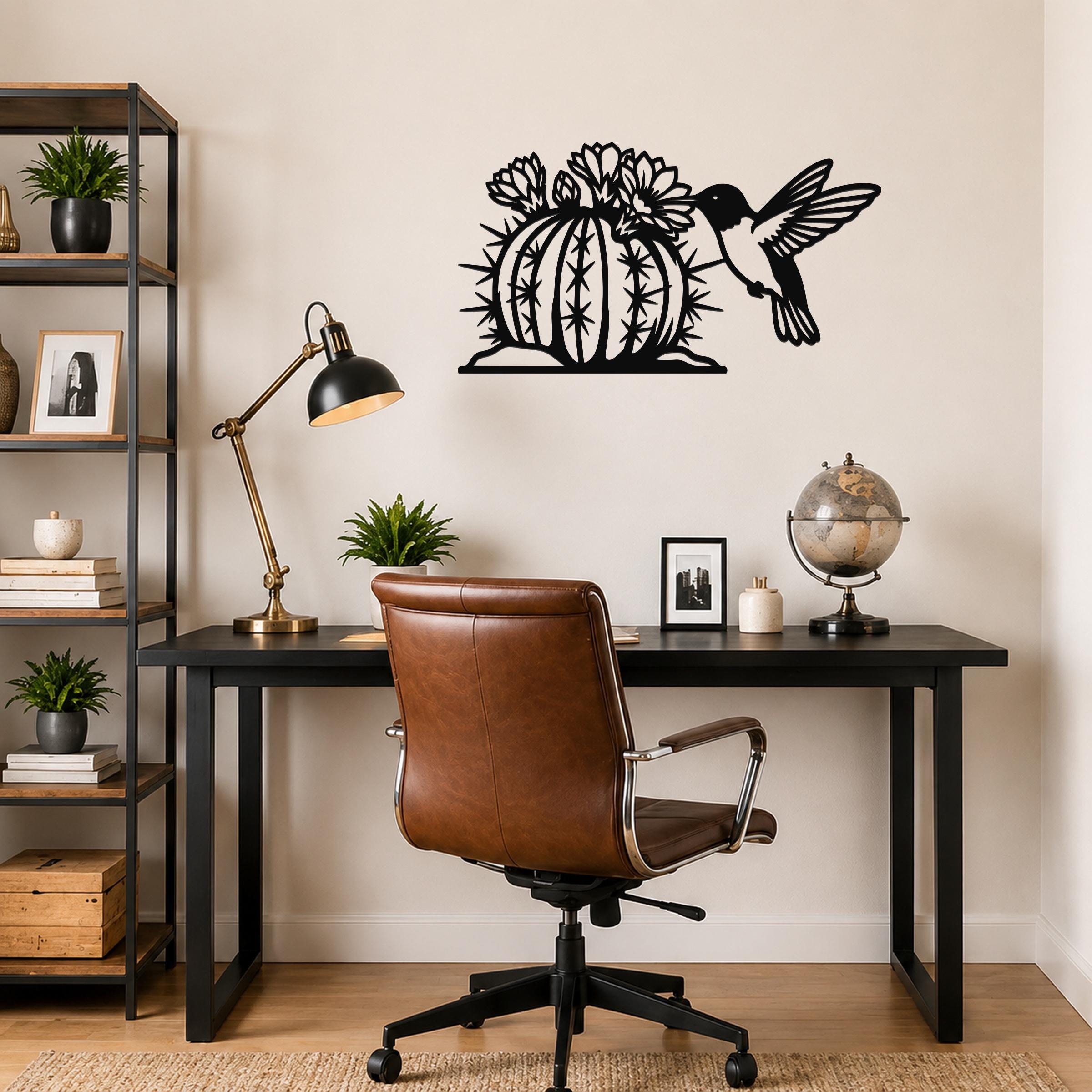 Black metal wall art featuring a hummingbird and flowering barrel cactus cutout, mounted above a black desk in a home office.