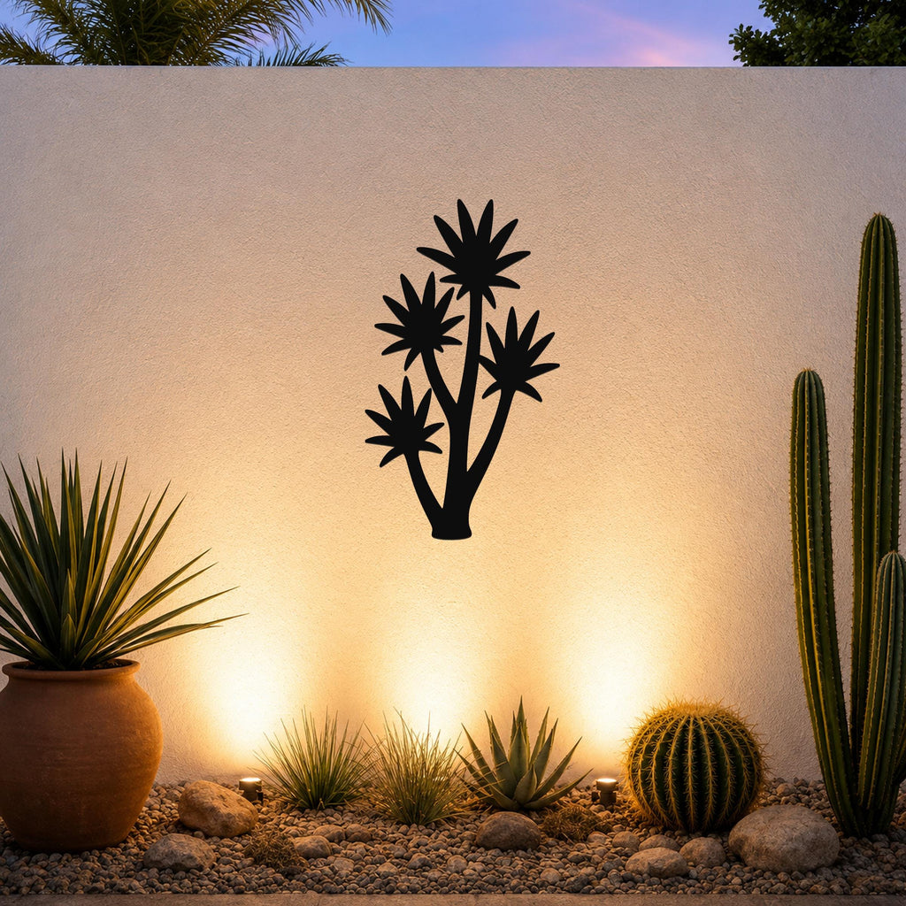 Black metal yucca wall art with multiple star-shaped leaf cutouts, mounted on a textured outdoor wall above a desert garden with cacti and warm uplighting.