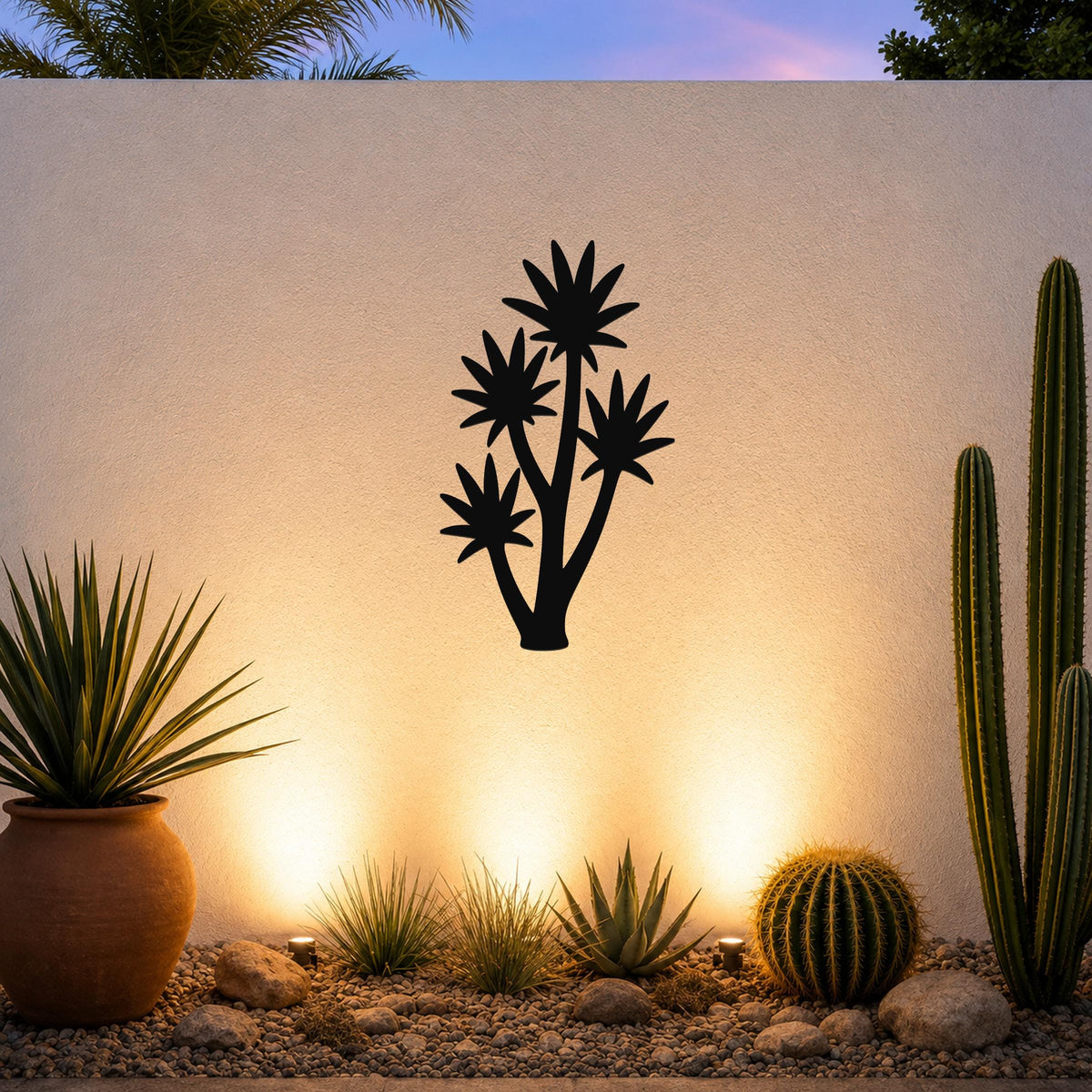 Black metal yucca wall art with multiple star-shaped leaf cutouts, mounted on a textured outdoor wall above a desert garden with cacti and warm uplighting.
