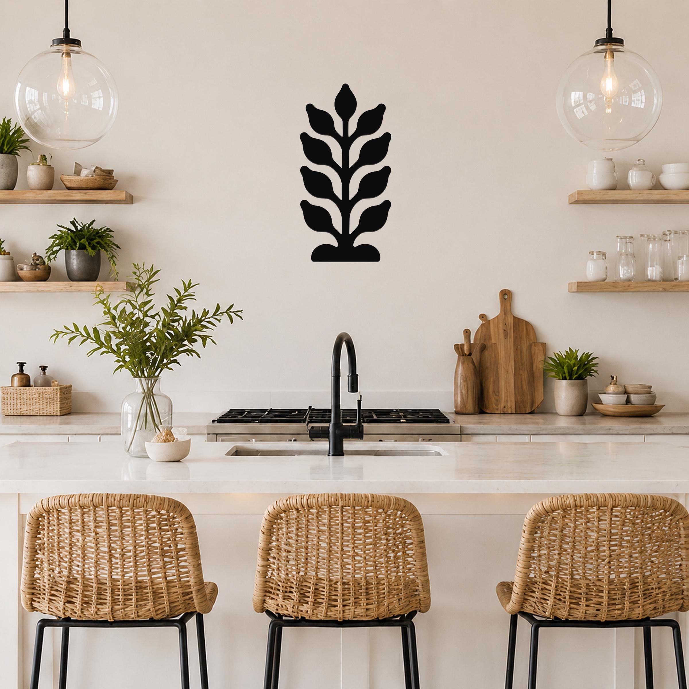 Black metal wall art with a leafy plant silhouette, mounted on a kitchen wall above a counter between two glass pendant lights.