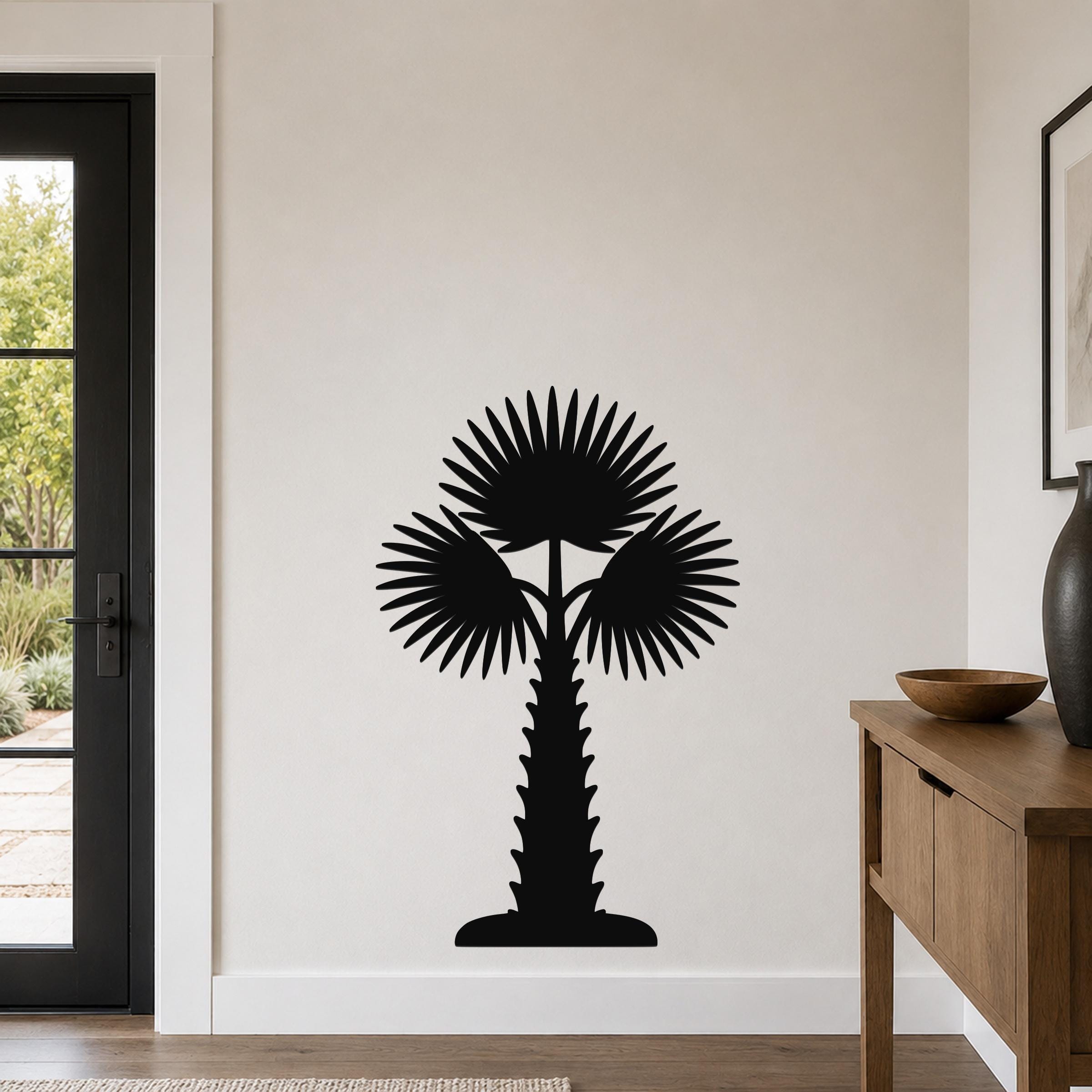 Black metal palm tree wall art with fan-shaped fronds and a textured trunk, mounted on a light-colored wall in a modern entryway.