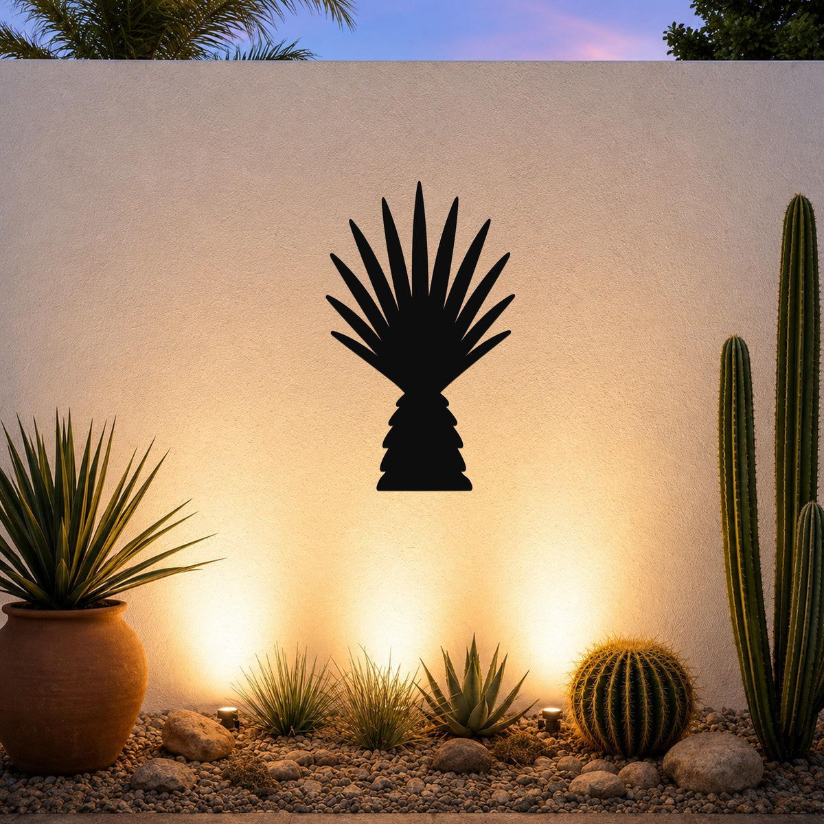 Black metal wall art cutout of a fan palm tree silhouette, mounted on a white outdoor wall above a desert garden with cacti and warm ground lighting.