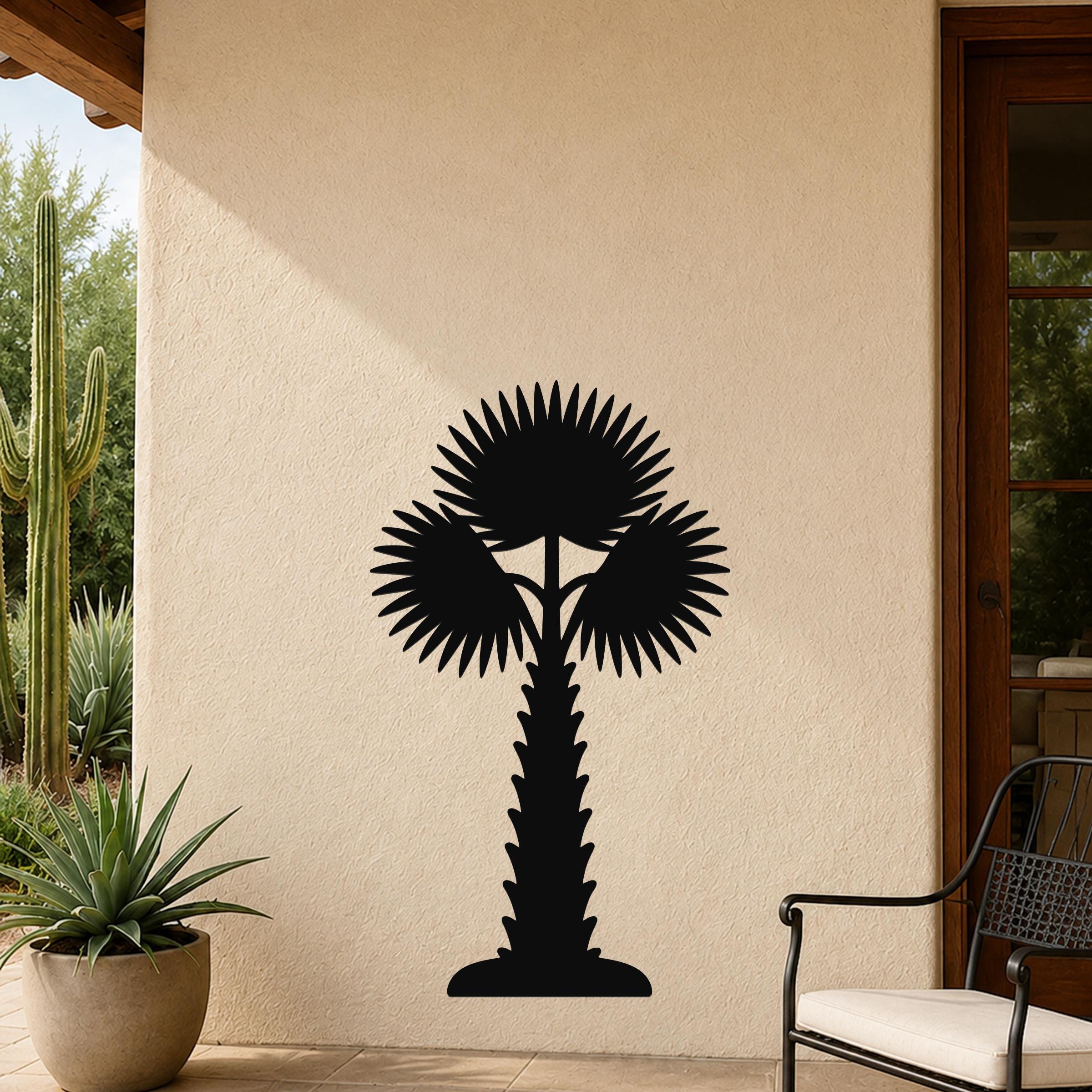 Black metal palm tree wall art with fan-shaped fronds and a textured trunk, mounted on an outdoor patio wall beside a potted succulent and a wooden door.