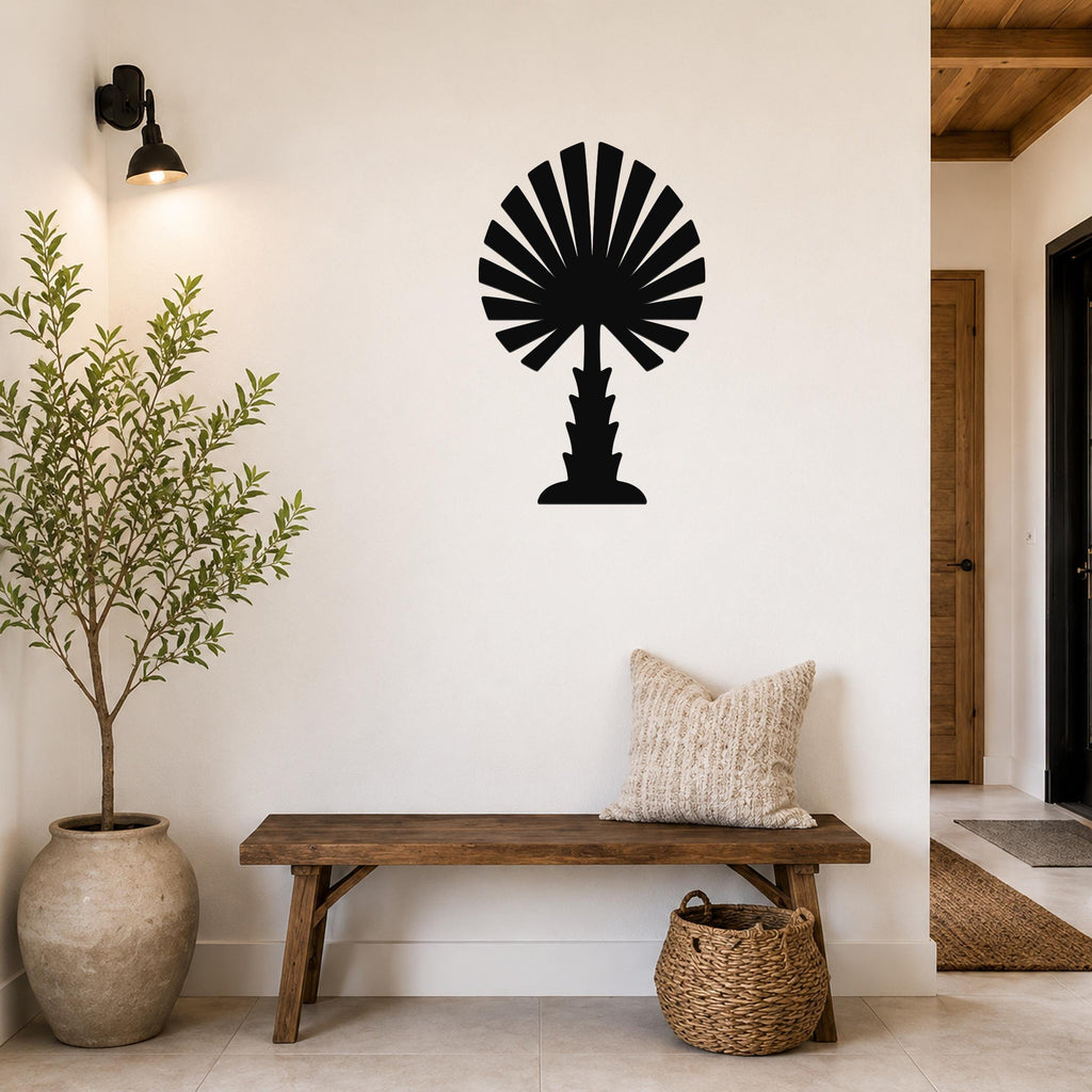Black metal palm tree wall art with fan-shaped fronds, mounted on a white wall above a wooden bench in a entryway.