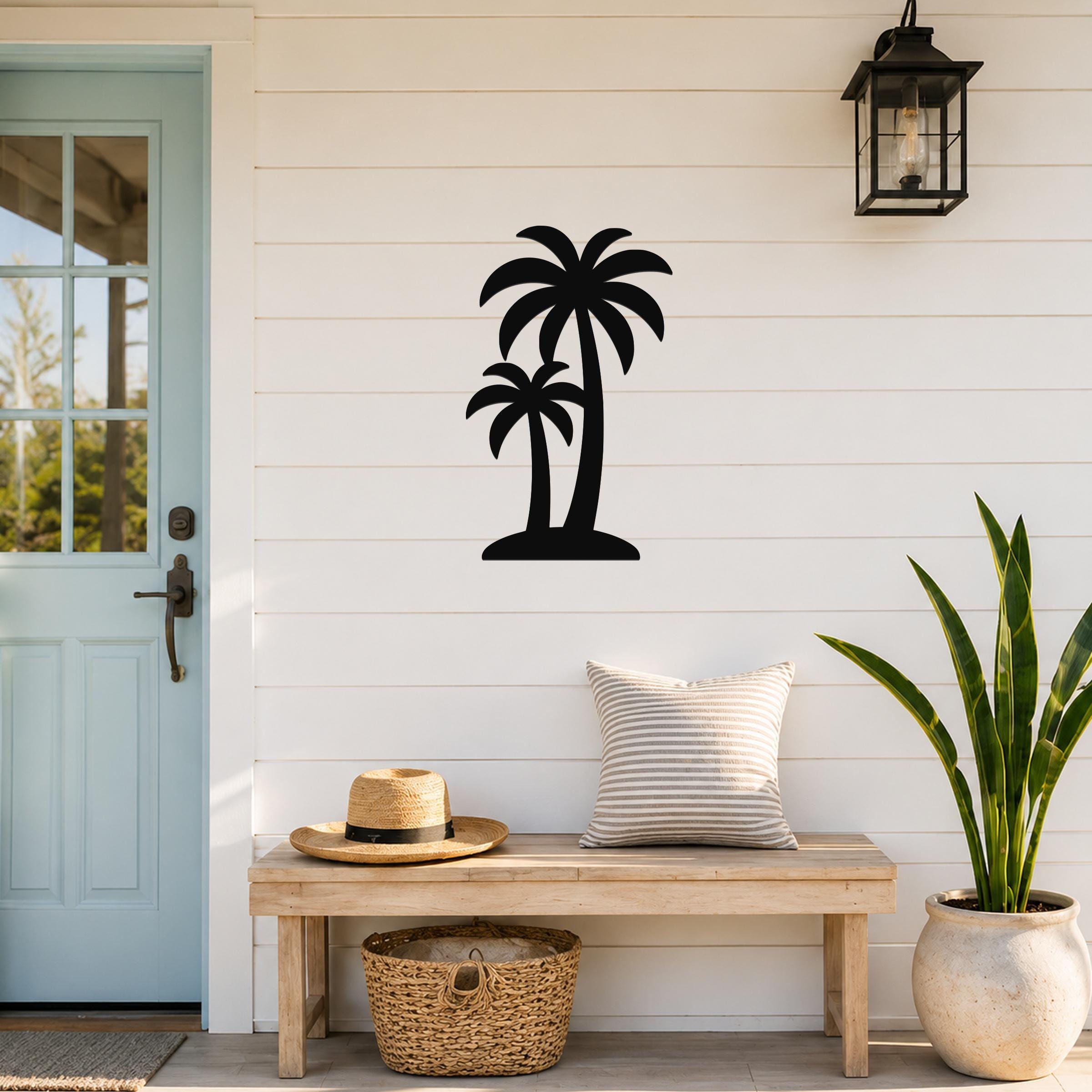 Black metal twin palm tree wall art silhouette mounted on a white shiplap wall above a wooden bench in a porch entryway.