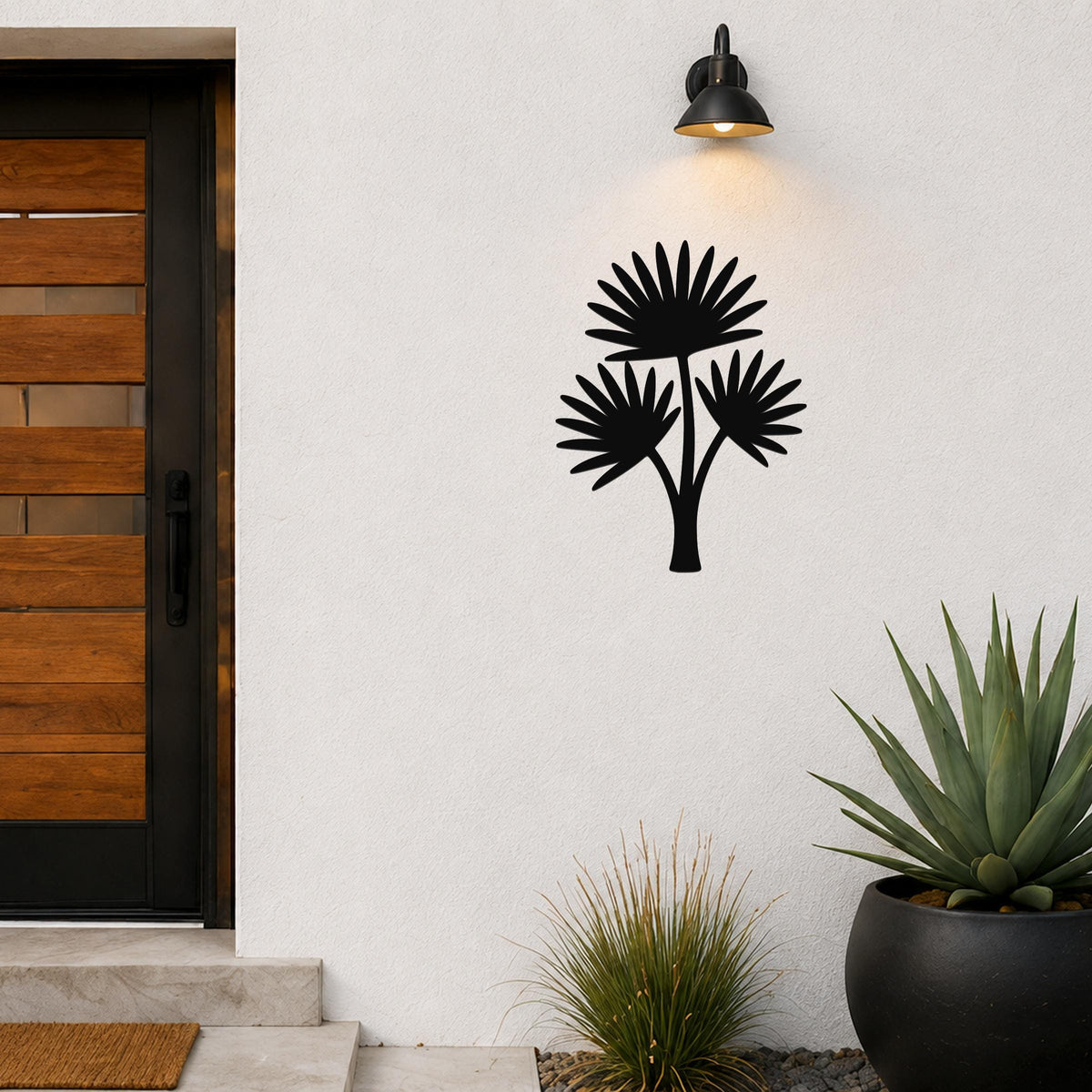 Black metal cutout palm tree wall art with three fan-shaped fronds, mounted on a white exterior wall above a potted succulent and near a modern front door.