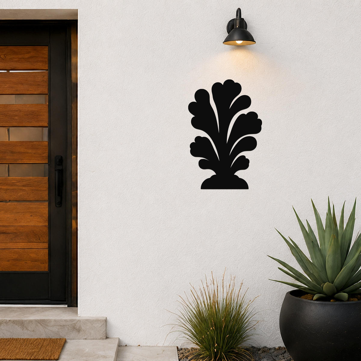 Black metal wall art in a coral or leaf-like silhouette, mounted on a white exterior wall beside a front door and potted plants.