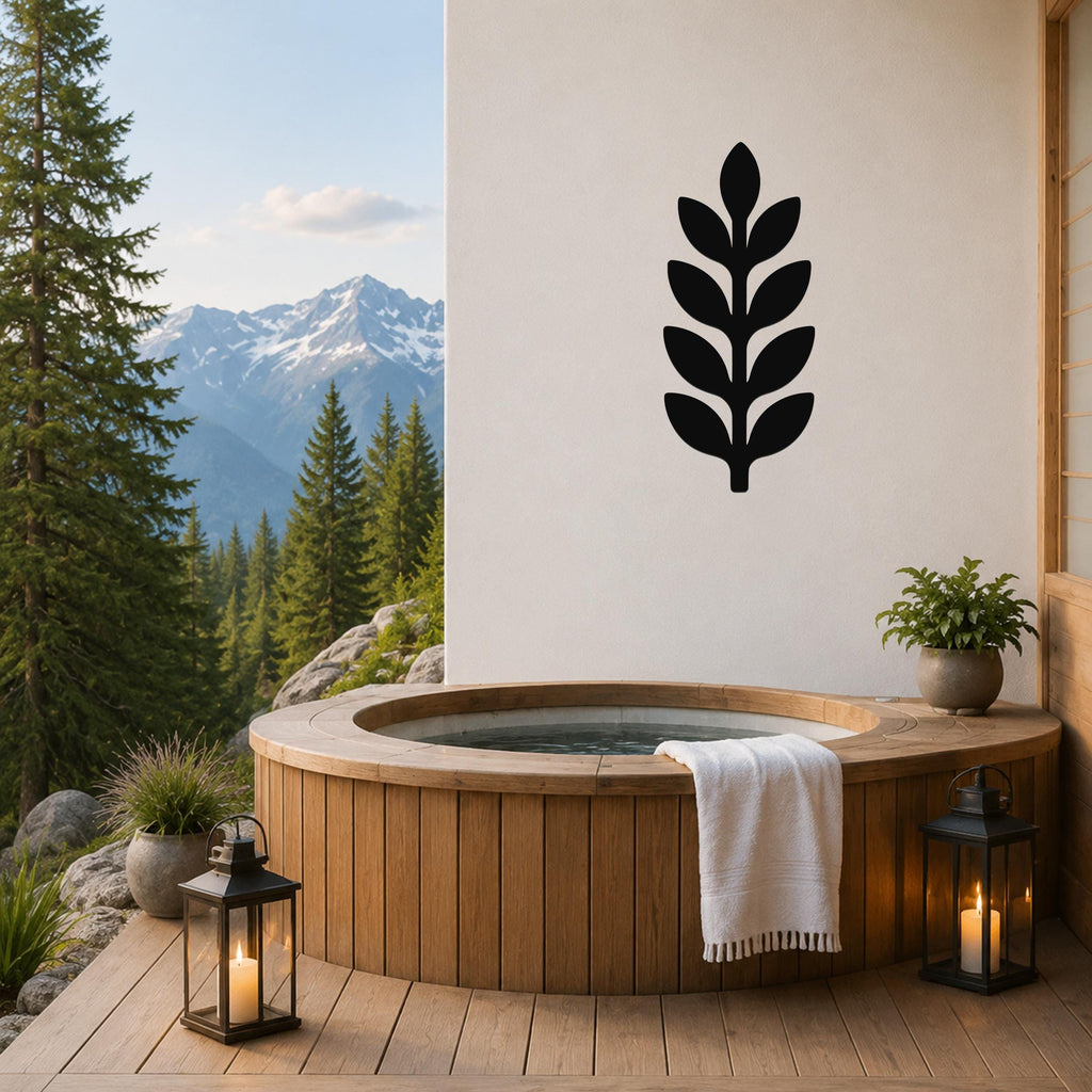 Black metal leaf sprig wall art with layered leaf cutouts, mounted on a white wall above a wooden hot tub on a mountain-view deck.