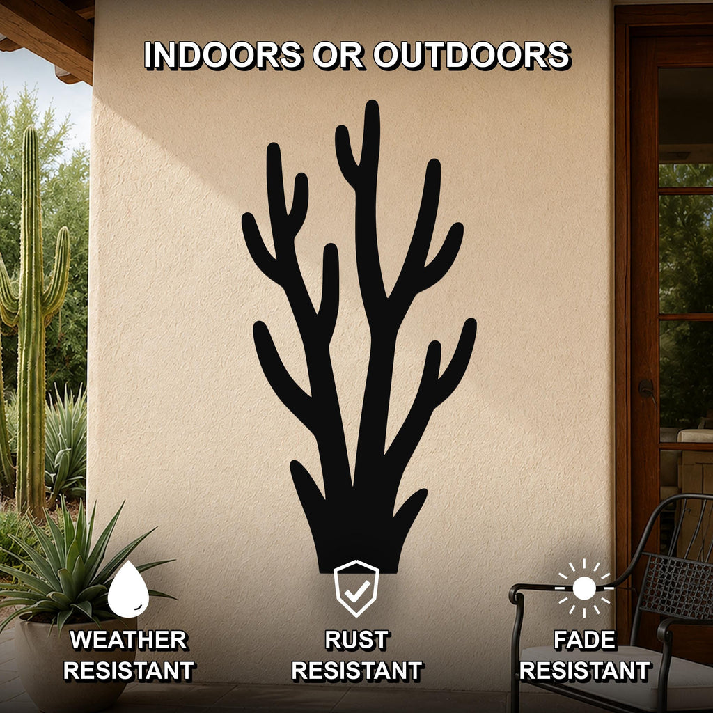 Black metal wall art in a desert branch silhouette, mounted on an outdoor patio wall with cacti and a chair visible nearby.