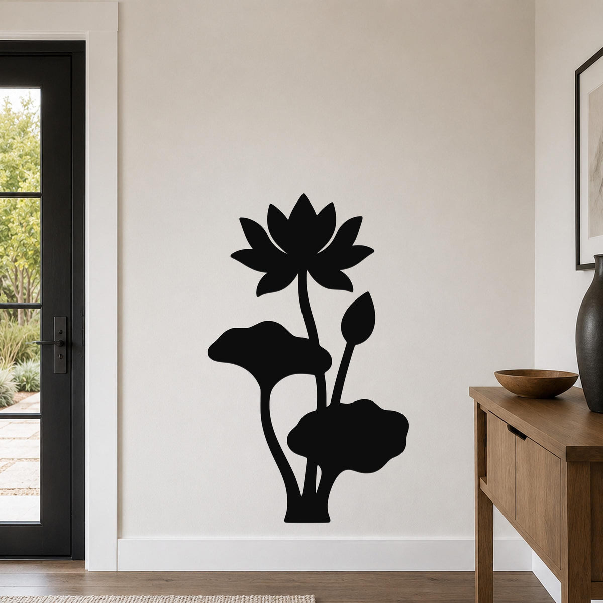 Black metal lotus wall art with flower and leaf cutouts, mounted on a light-colored wall in a modern entryway.